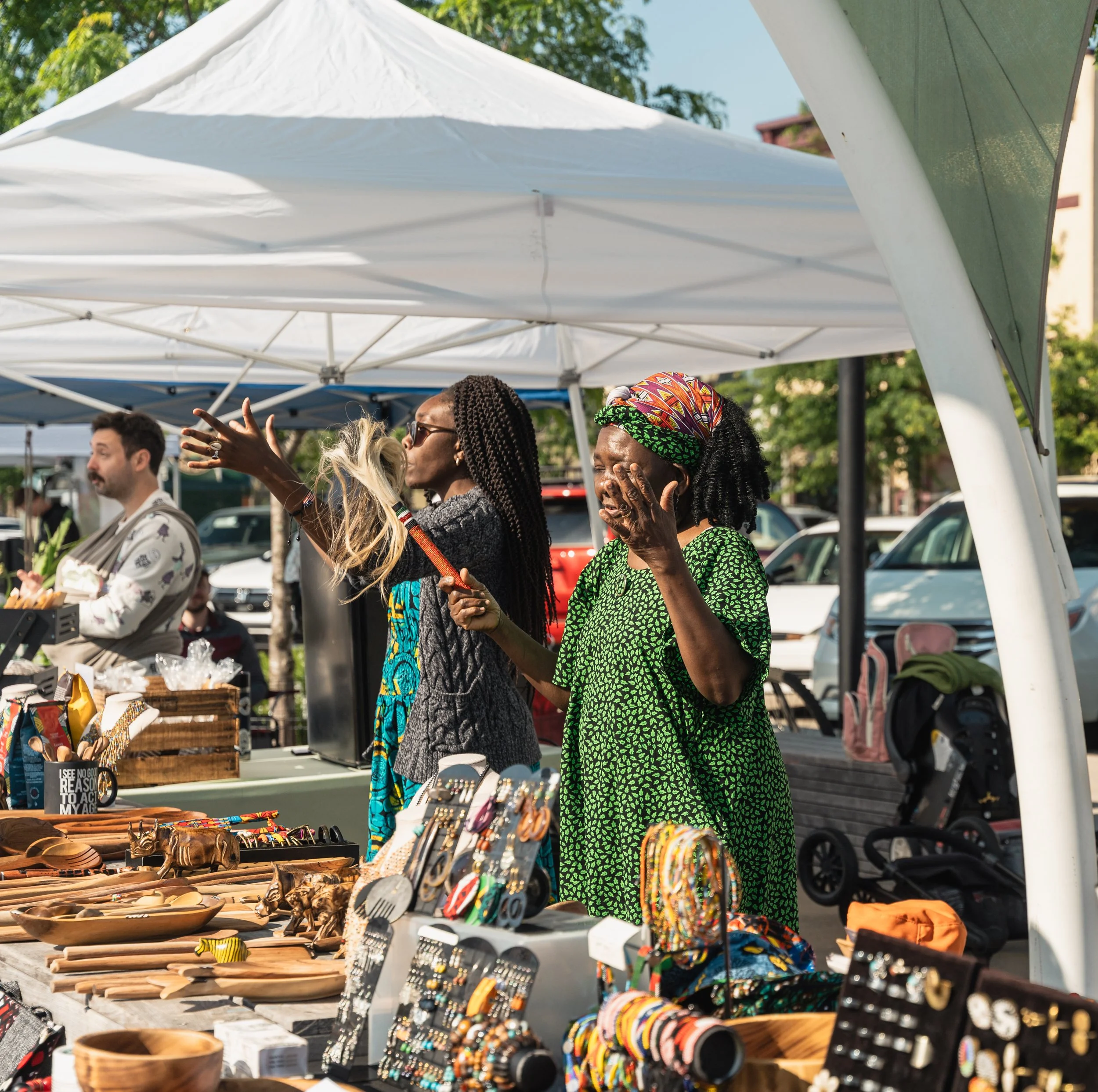 People shopping at an outdoor market stall with various jewelry, wooden and ceramic items on display.