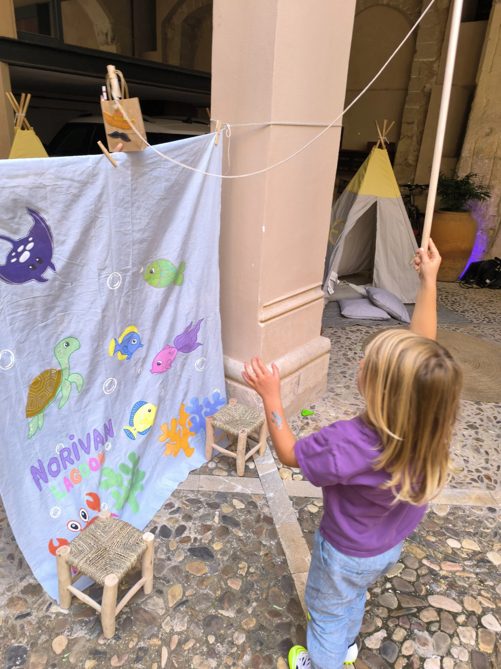 A little boy playing the traditional Scandinavian fiskedam fishing pond game, catching a goody bag behind a custom hand-painted "Norivan Lagoon" backdrop at a premium kids party in Palma, Mallorca by Norivan Kids Entertainment.
