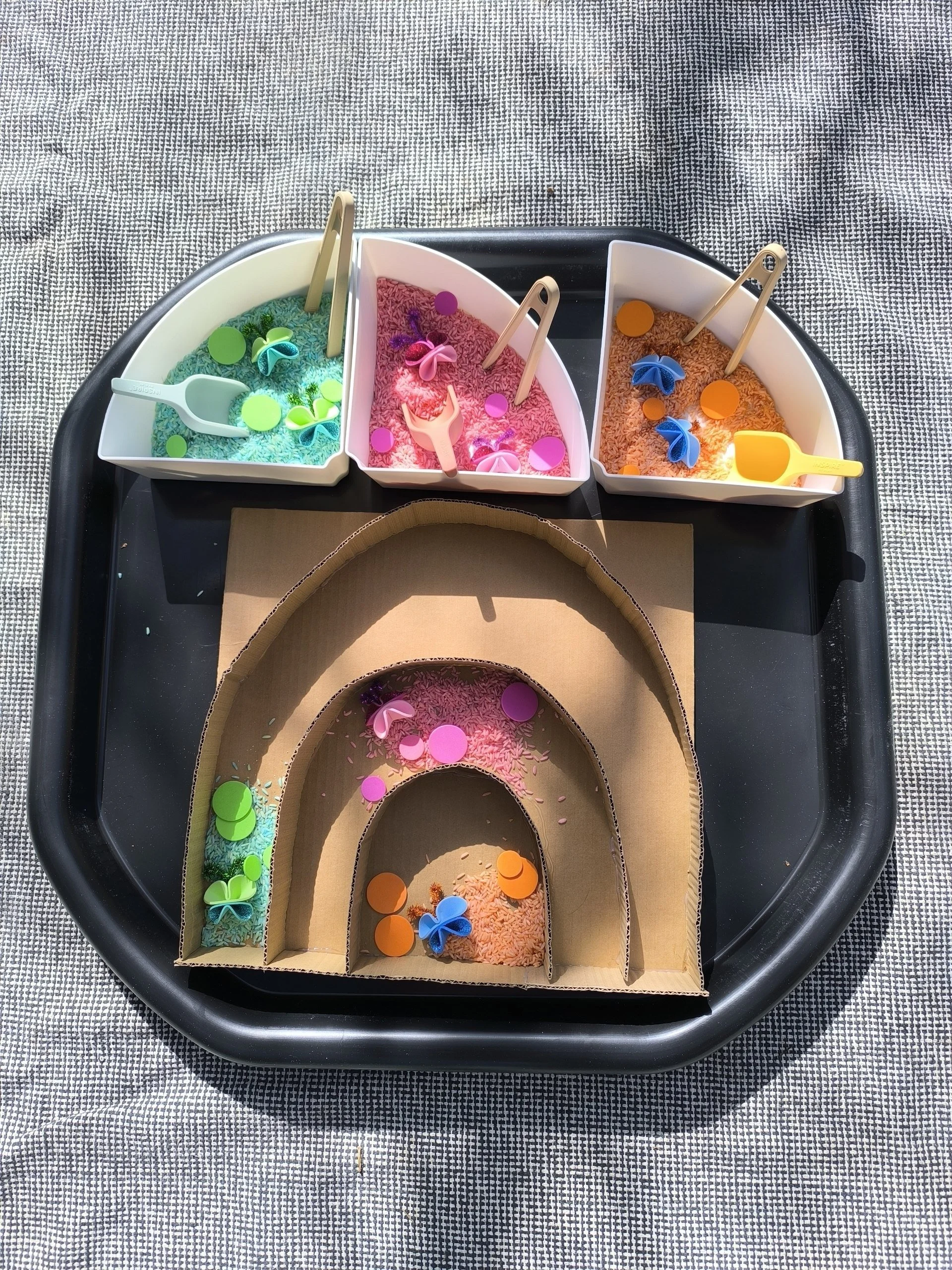 Creative sensory bin activity for kids featuring a handmade cardboard rainbow and vibrant colored rice at a premium children's party in Mallorca by Norivan Kids Entertainment.
