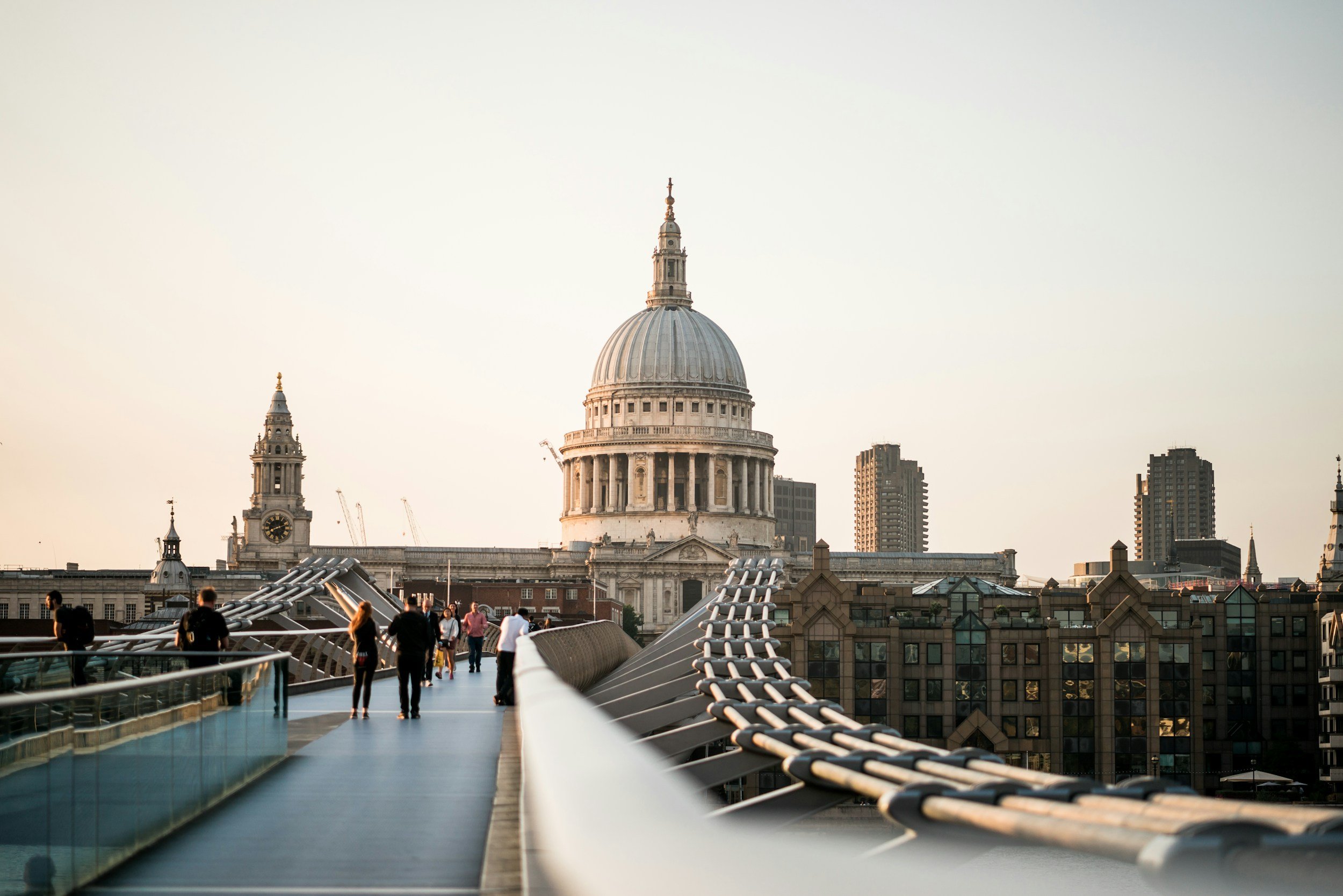 People walking on the Millennium Bridge in London with St. Paul's Cathedral in the background during sunset.