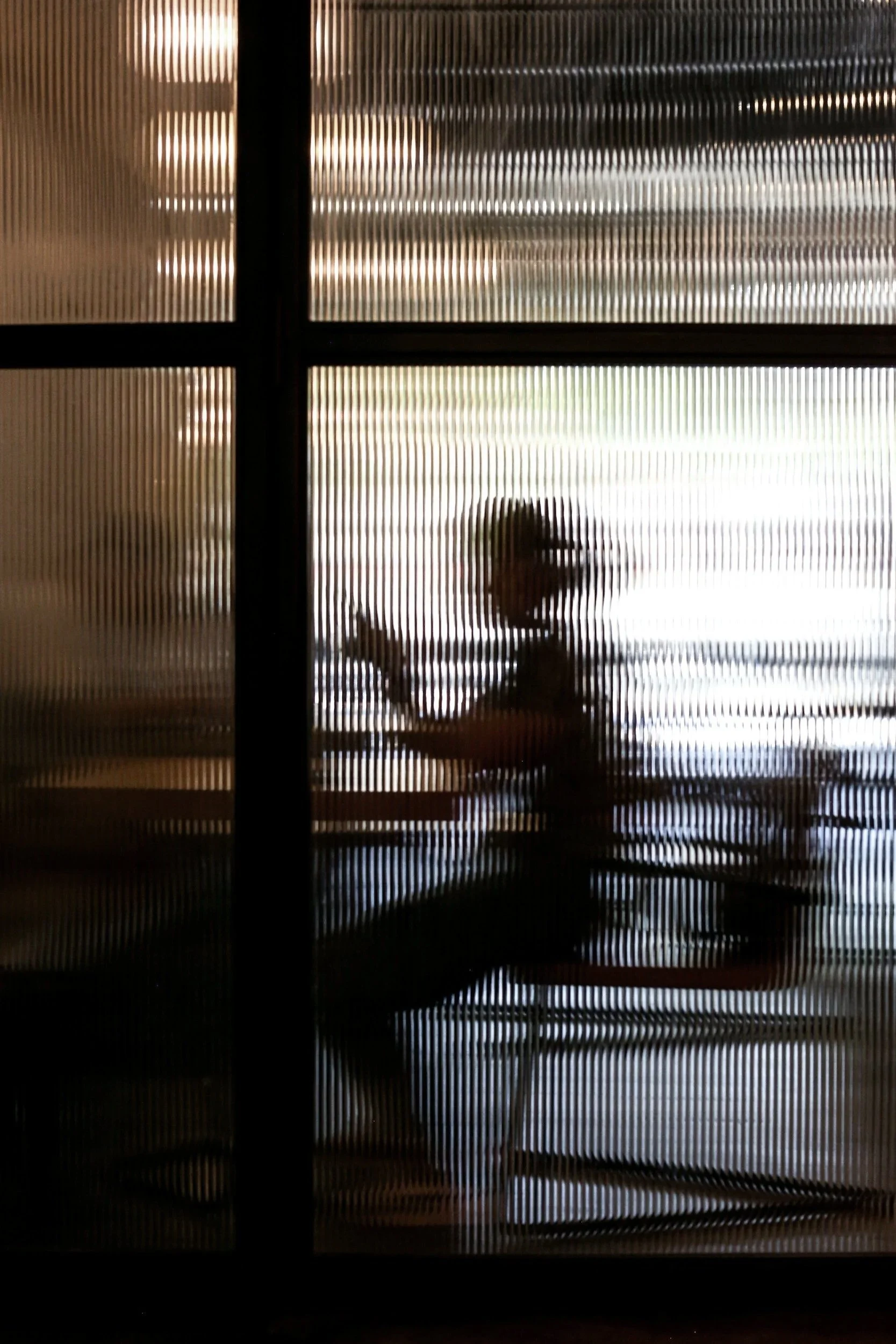 People walking with luggage outside near a building with vertical slats.