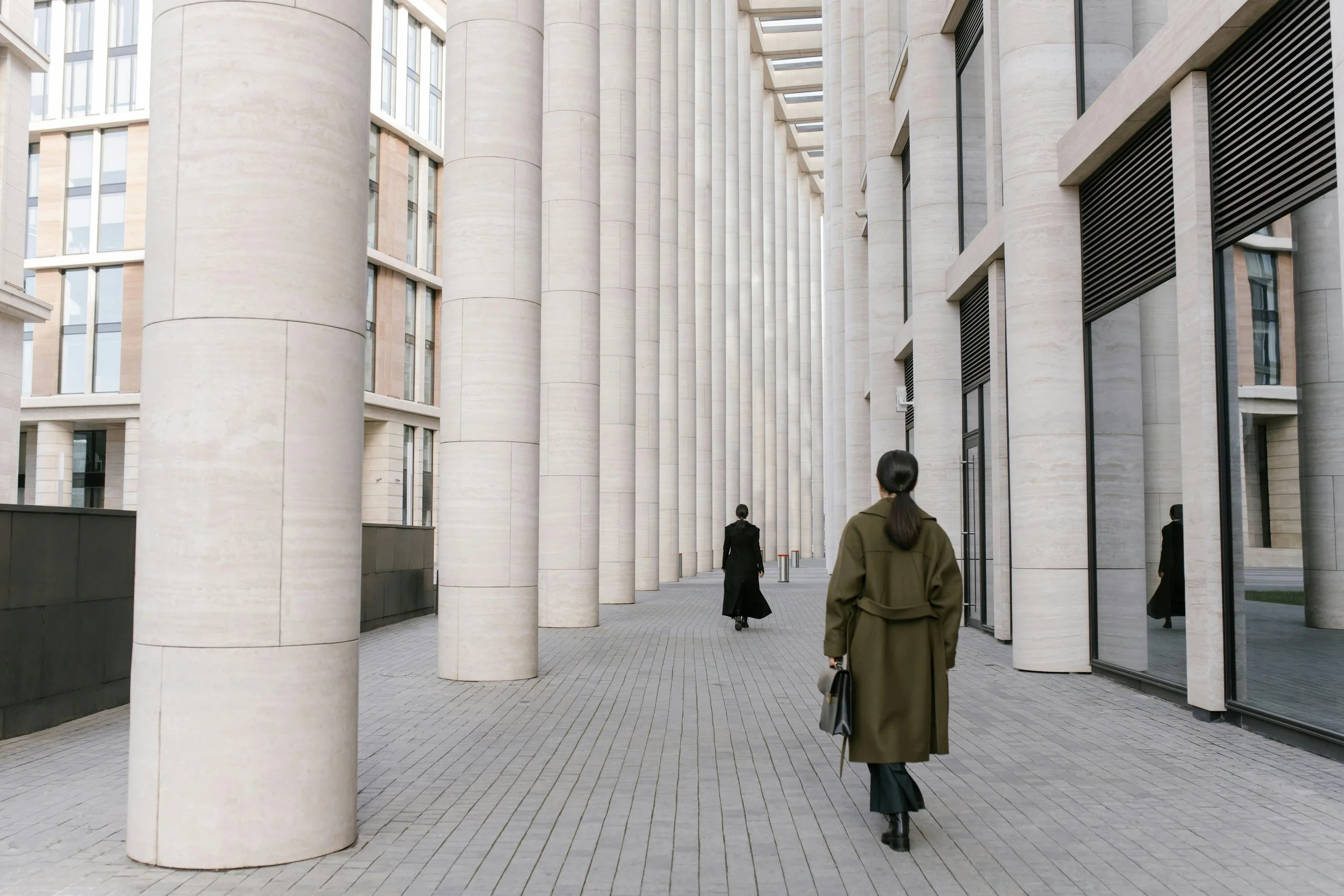 People walking in front of modern building with tall cylindrical columns and large windows.