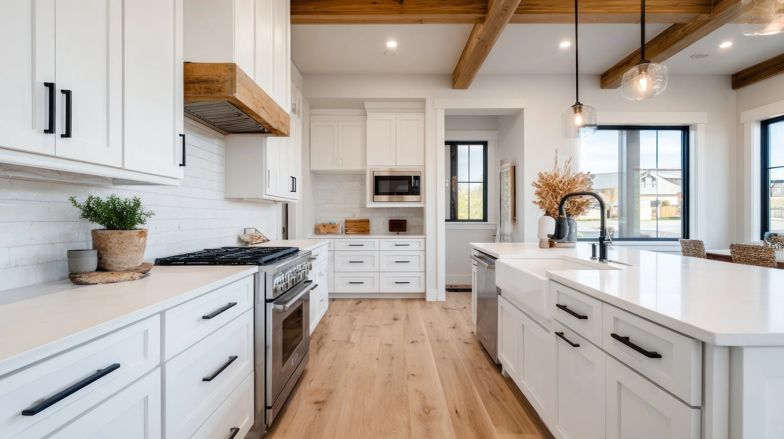 Modern kitchen with white cabinets, black handles, wooden accents, stainless steel appliances, and large windows with natural light.