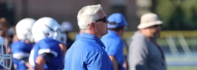 Football coach standing on sideline with players in blue helmets and jerseys in the background - Bexley Ohio Middle School Football OH 43209