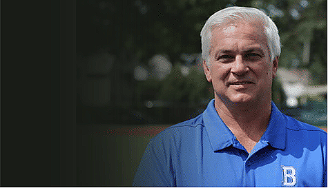 A middle-aged man with gray hair wearing a blue polo shirt with a 'B' logo stands outdoors in front of a blurred background.
