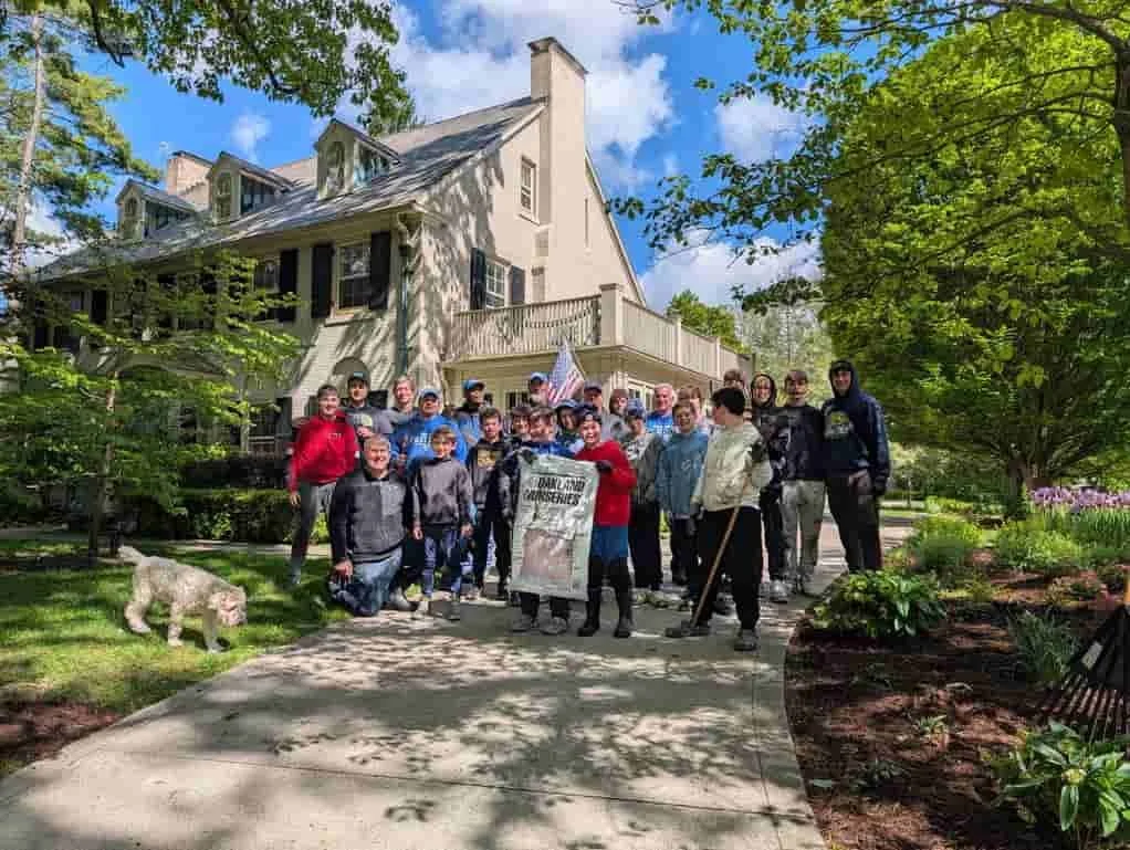 Bexley Middle School Football Team Community Service Bexley OH Ohio Bexley School Team standing on a sidewalk in front of a large, historic house with trees and a garden around it, some holding a banner and an American flag.