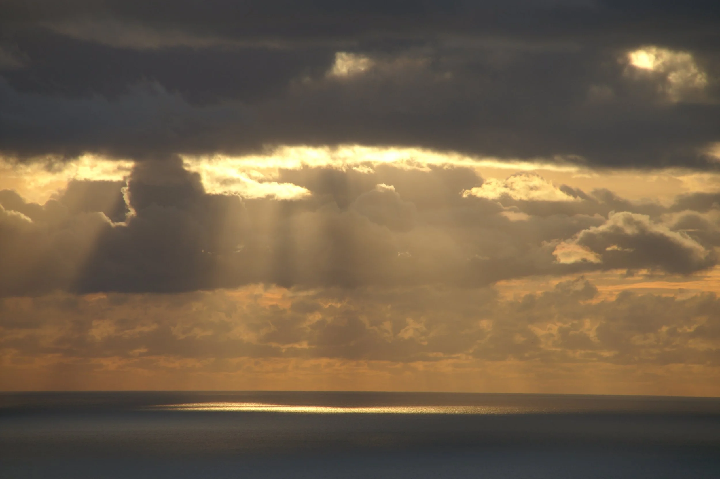 Sunlight breaking through dark clouds over the ocean during sunset.