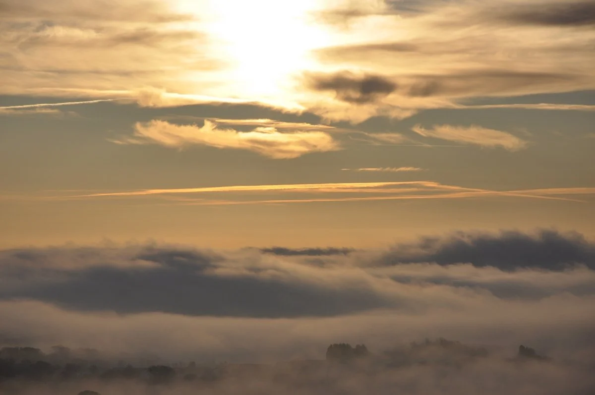 Sunrise or sunset over a foggy landscape with clouds and trees in the distance.