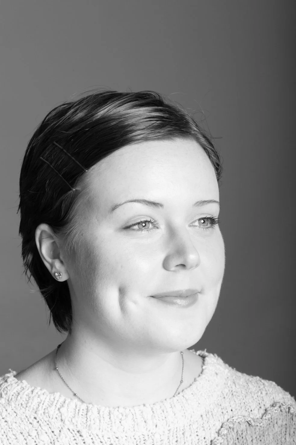Black and white portrait of a woman with short dark hair, wearing earrings, a necklace, and a textured sweater, looking slightly to the right with a gentle smile.