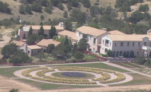 Aerial view of a residential area with large white houses, trees, and a landscaped roundabout with a spiral garden in the foreground.