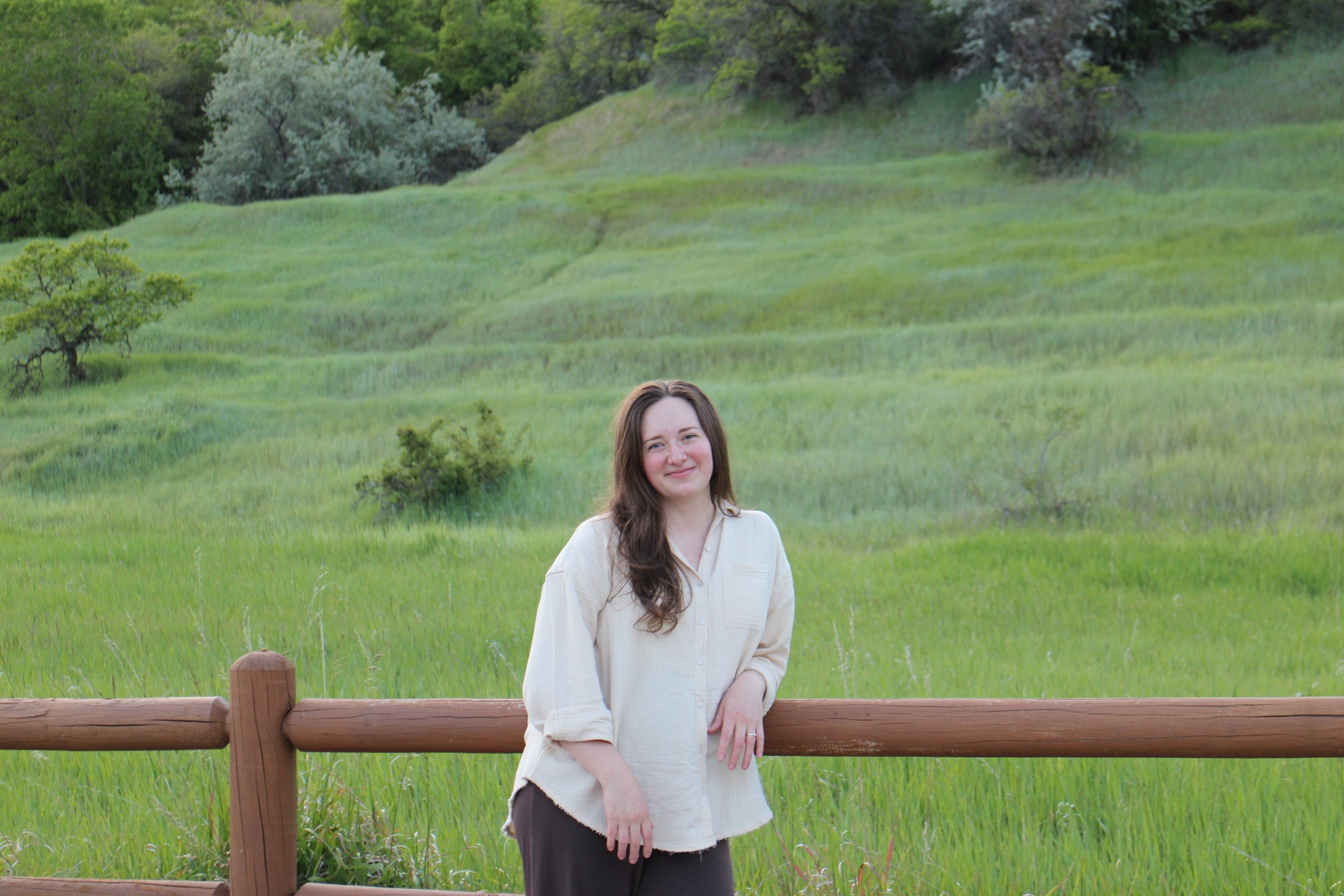 EMDR therapist leaning against a wooden fence in a peaceful mountain meadow