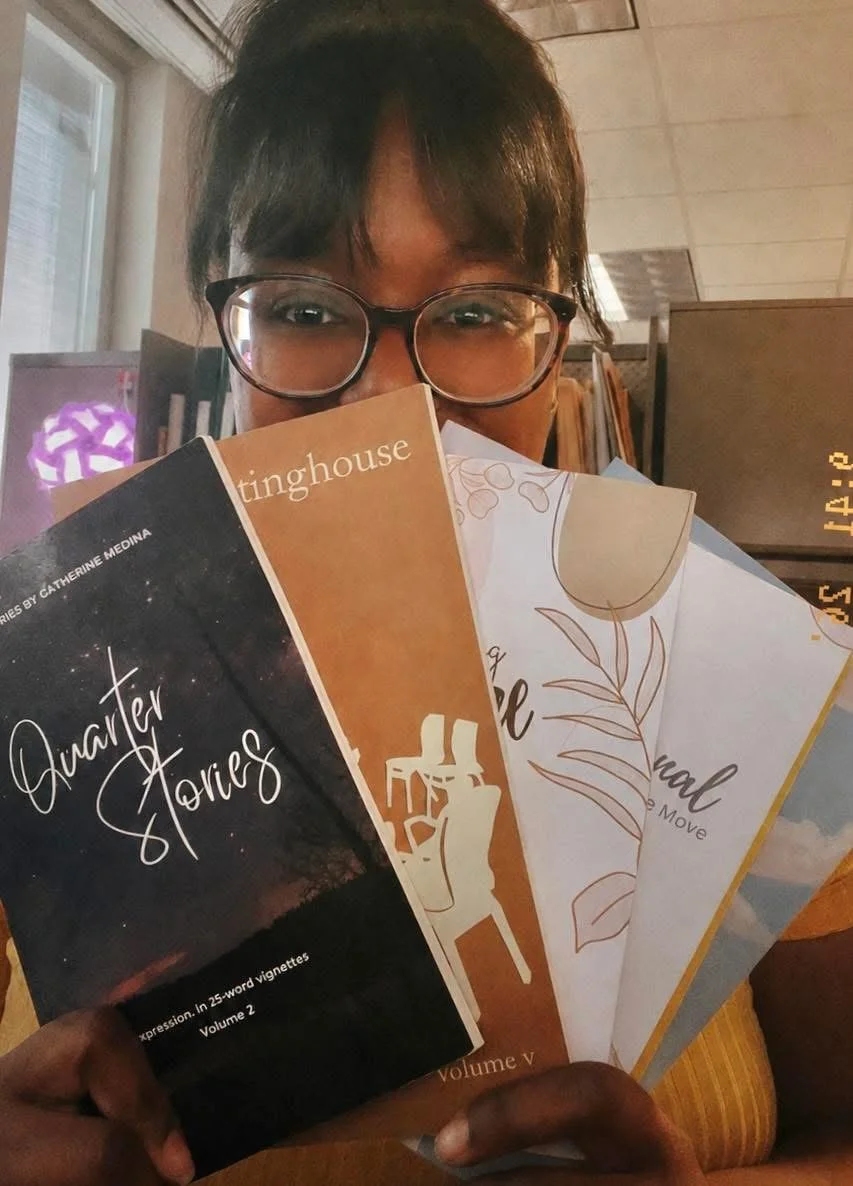 A person with glasses holding several books in front of their face, showing only their eyes and forehead. The books are titled 'Quarter Stories,' \Writing Journal,' and others with decorative covers.