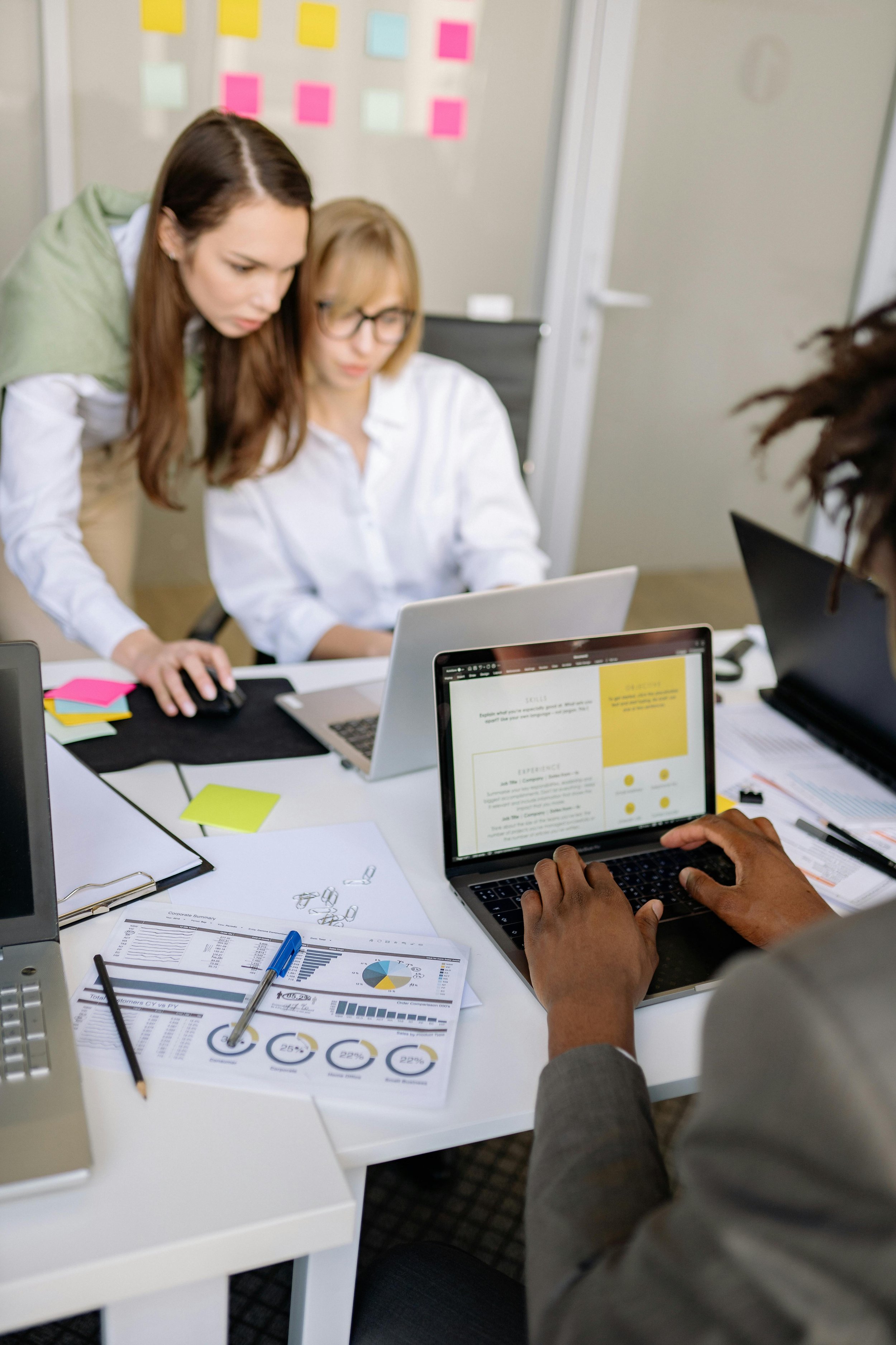 People working together at a desk with laptops, papers, and charts in a modern office setting.