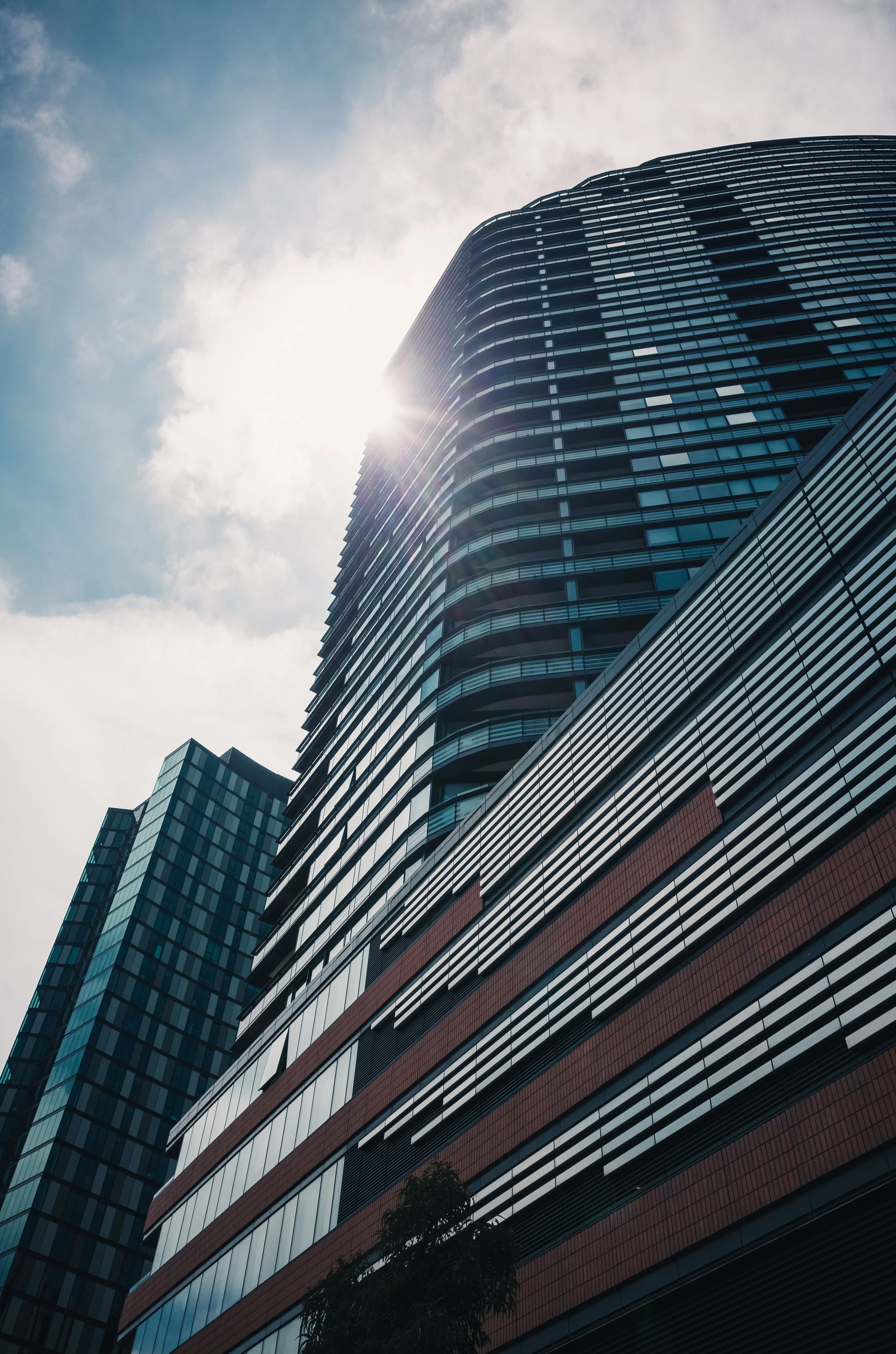 A tall modern glass skyscraper reflecting the sky and sun, with other buildings visible nearby.