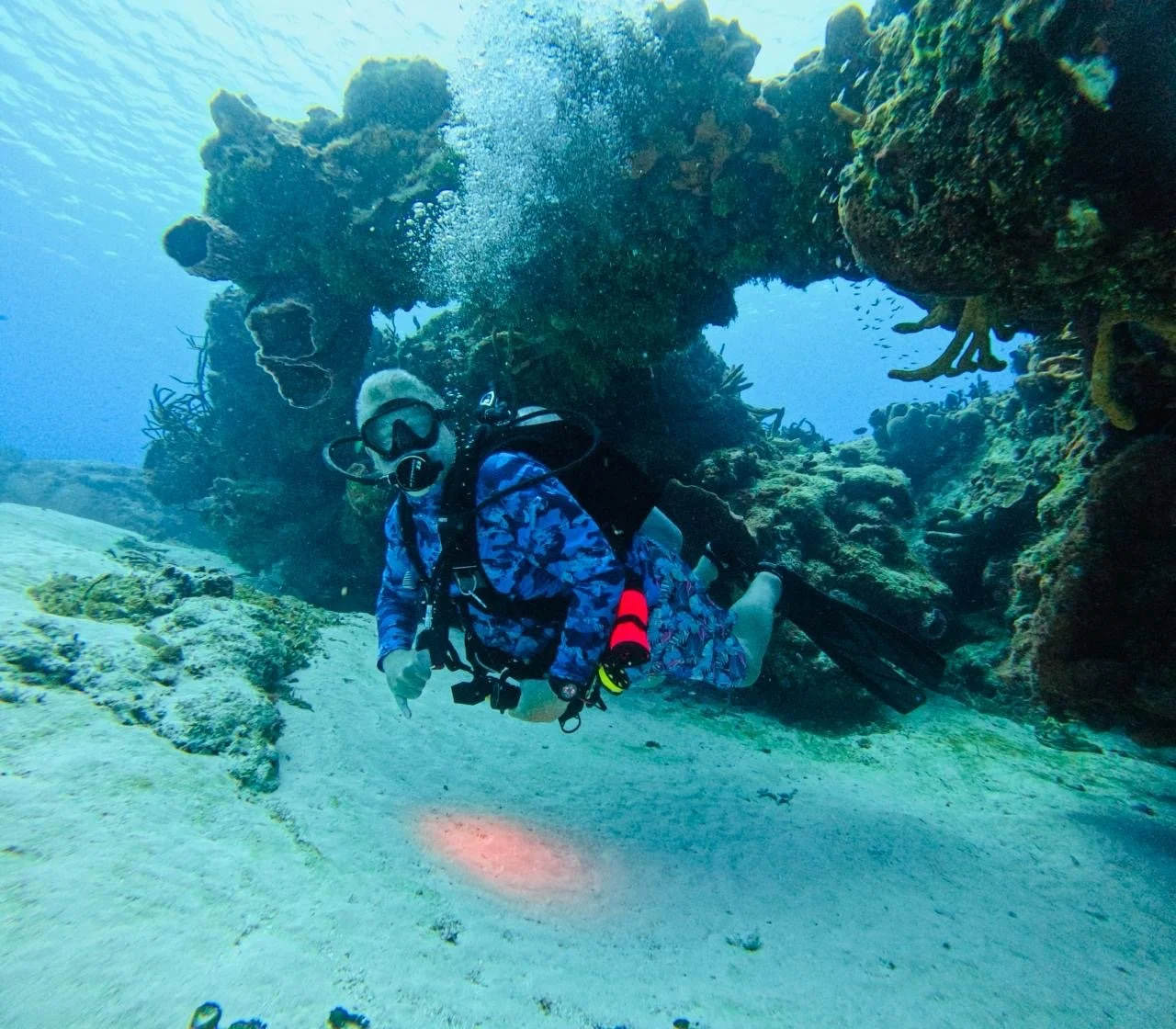 An underwater diver in scuba gear exploring a coral reef with rocky formations.