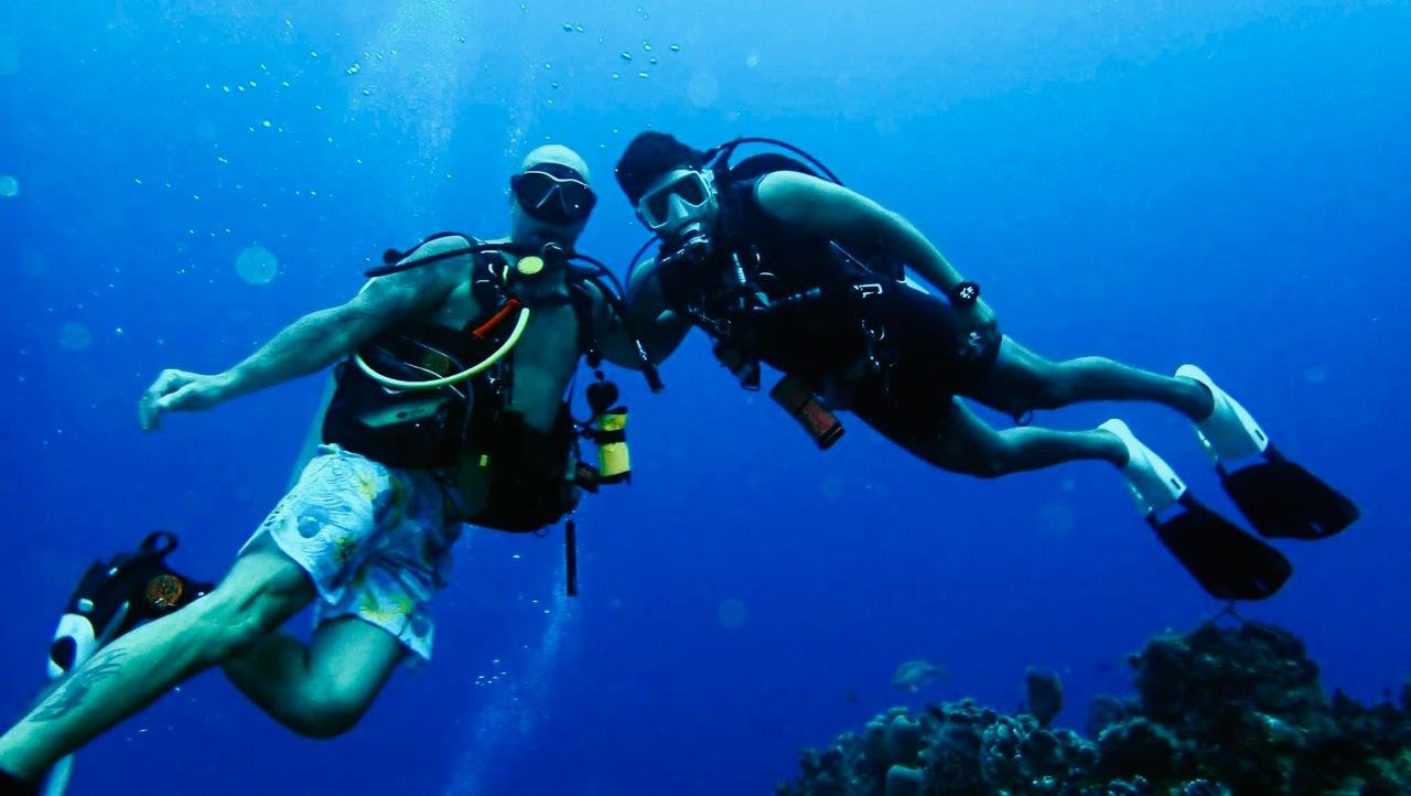 Two scuba divers underwater, wearing masks and fins, swimming near coral reef.
