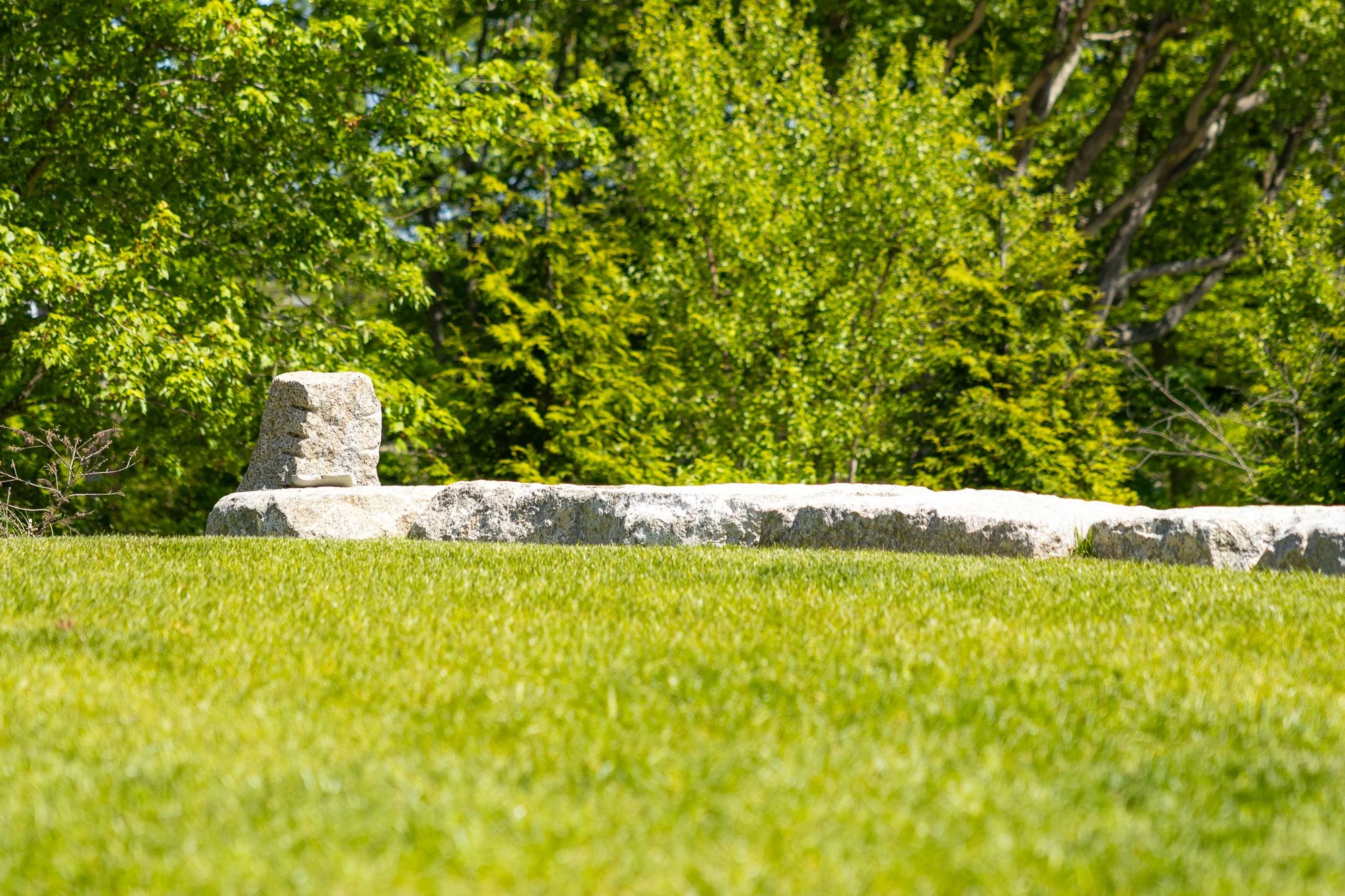 A stone structure on a grassy field with green trees in the background.