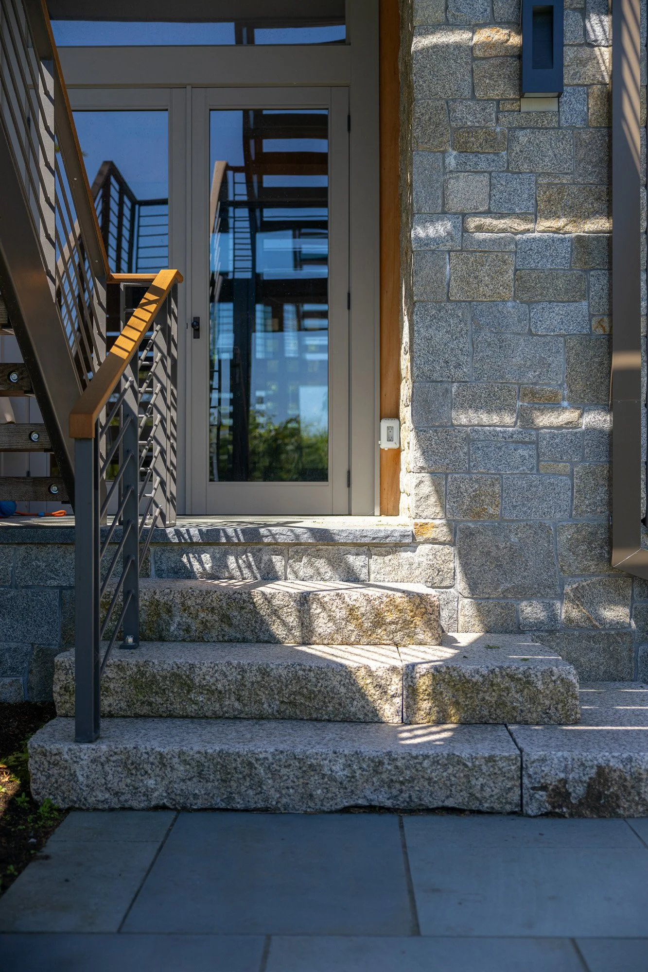 Stone steps leading to a glass door entrance of a modern building with metal and wood railing on the side.