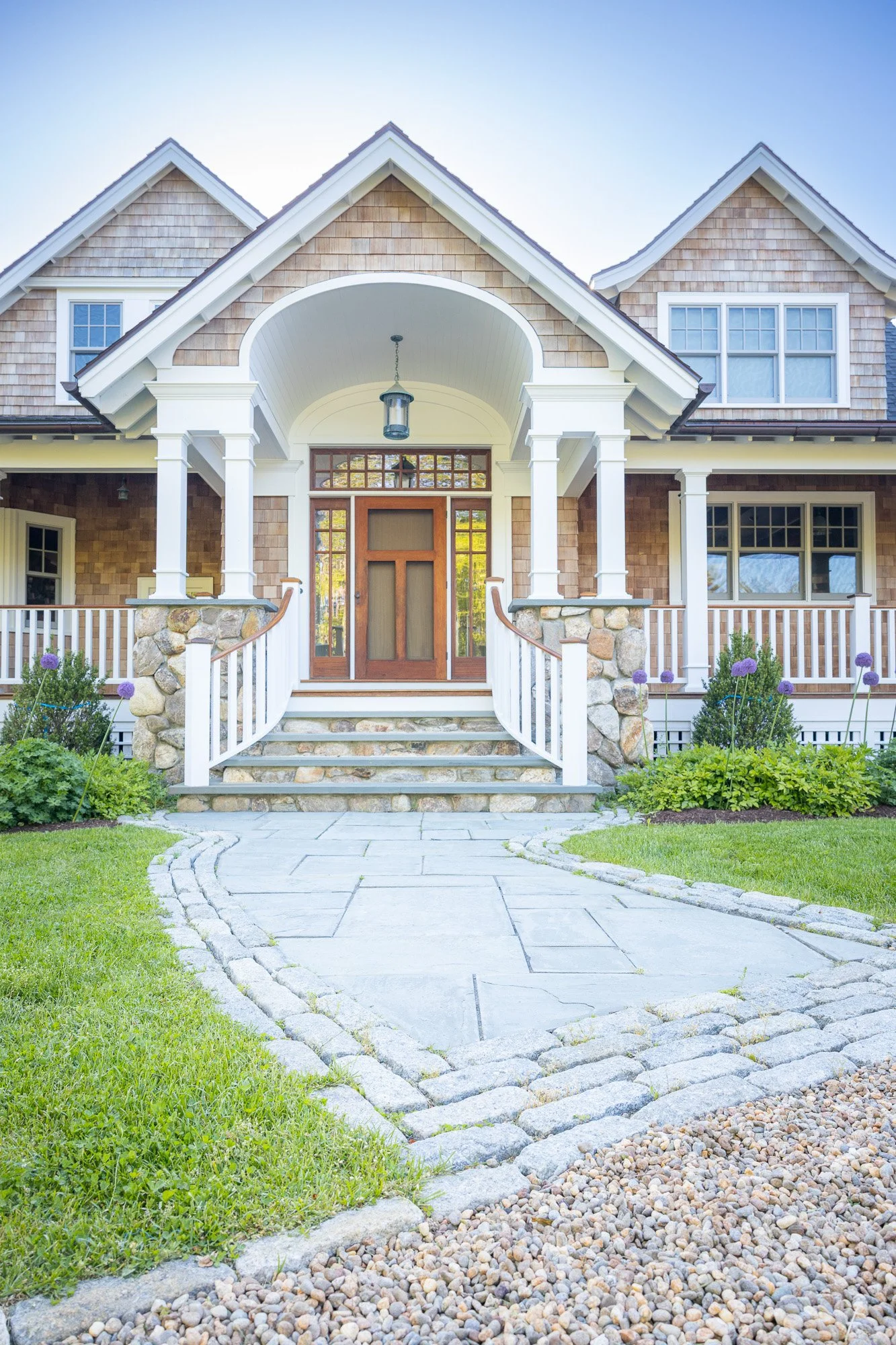 Front view of a house with a stone pathway leading to the front door, a well-maintained green lawn, and landscaped flower beds with purple flowers.