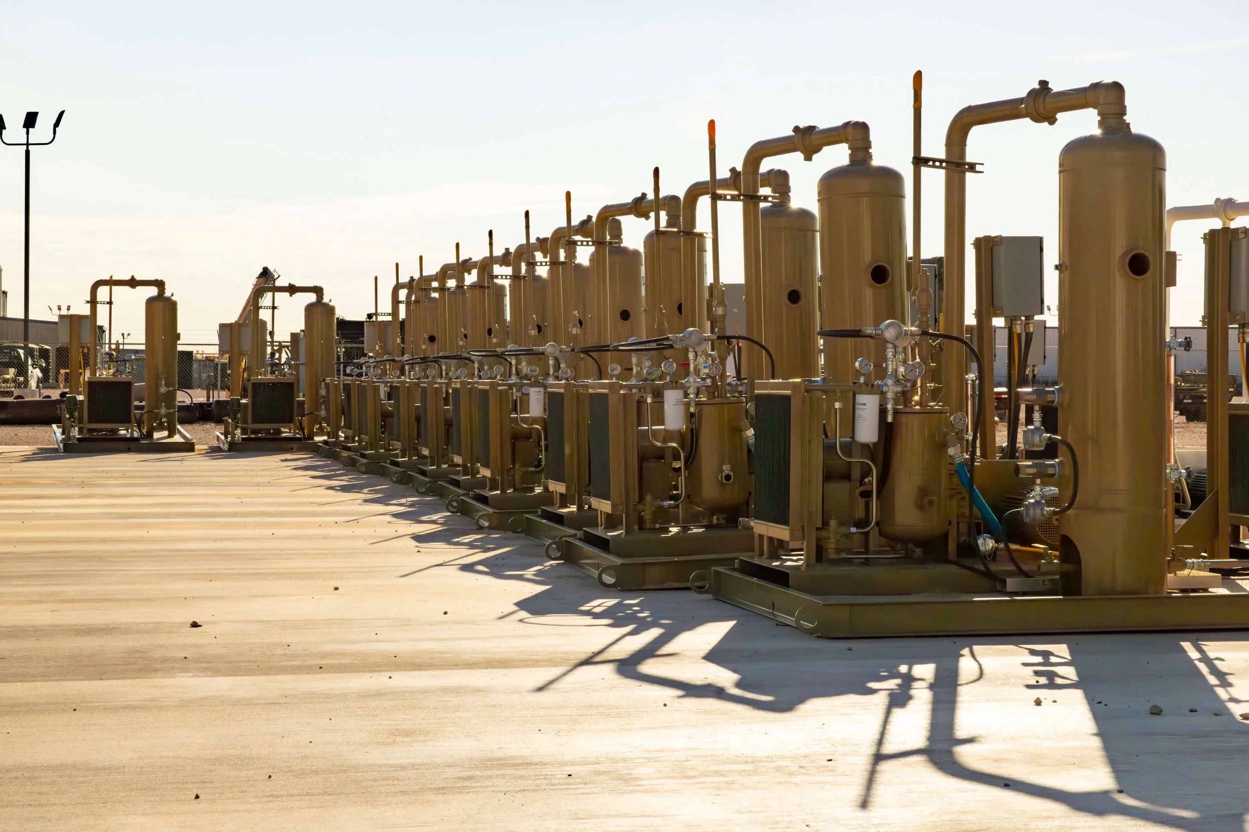 Industrial facility with large yellow tanks and piping, set on a concrete platform under a clear sky.