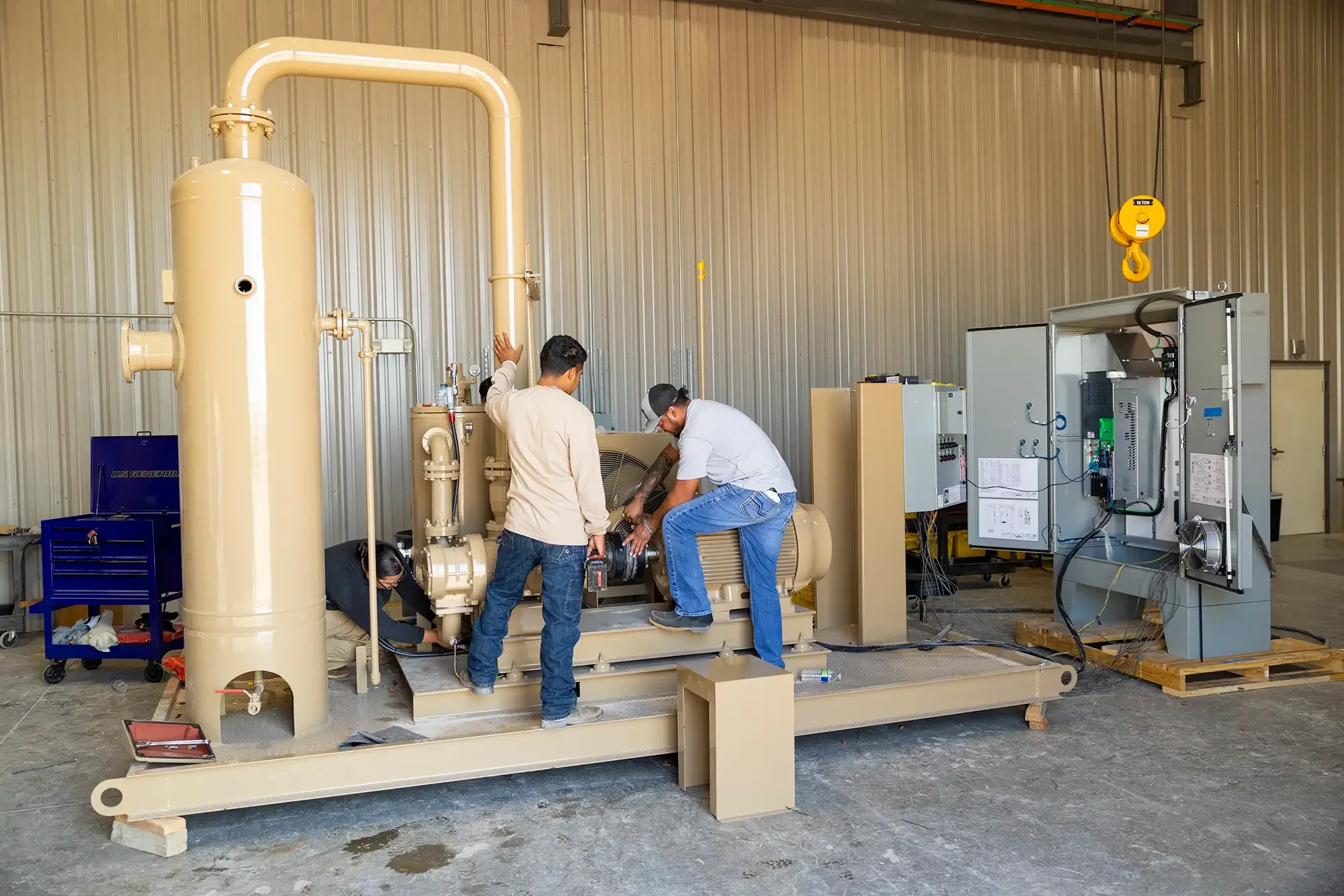 Workers repairing or maintaining a large industrial generator inside a warehouse with metal walls.