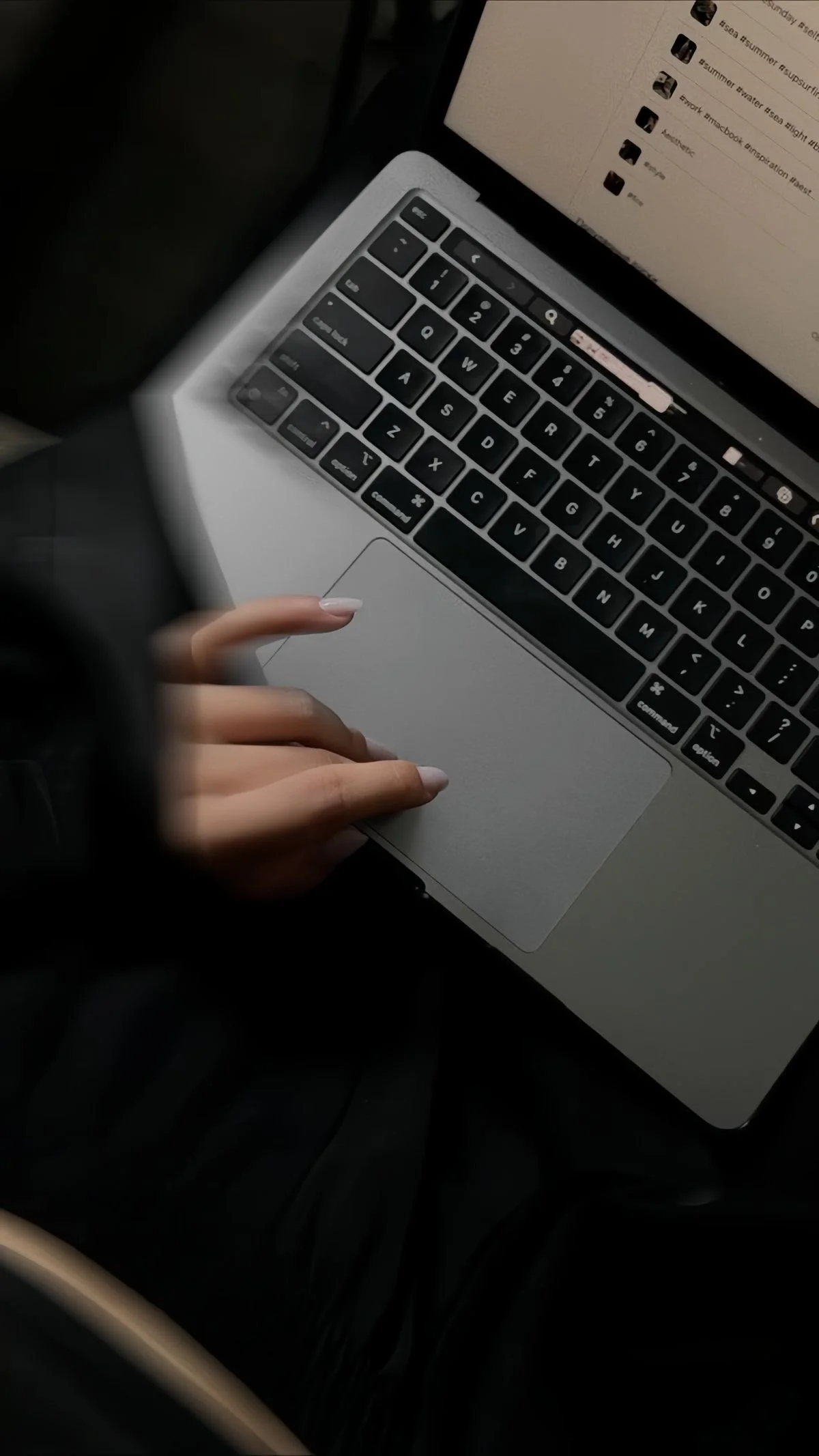 A person's hand resting on the trackpad of a silver laptop with a black keyboard. The laptop screen displays a document or webpage with text and file icons.