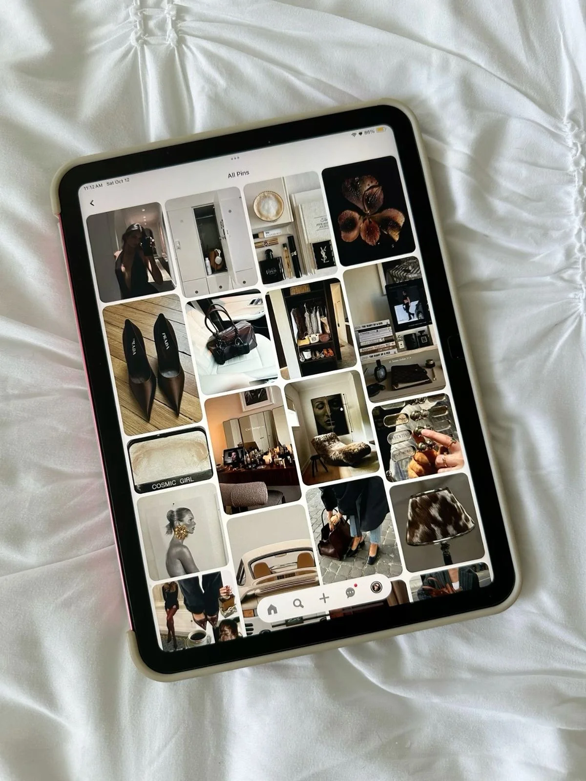 An iPad displaying a Pinterest board with various images of fashion accessories, home decor, and art, resting on a white satin fabric.