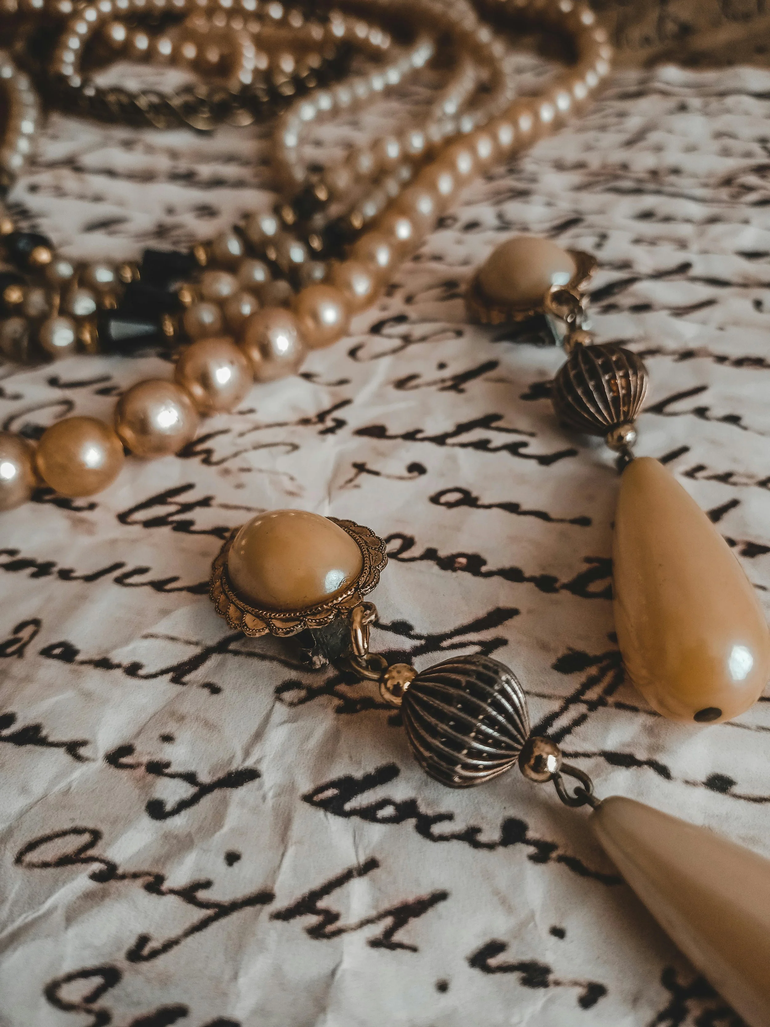 Close-up of pearl and metal jewelry resting on handwritten script paper.