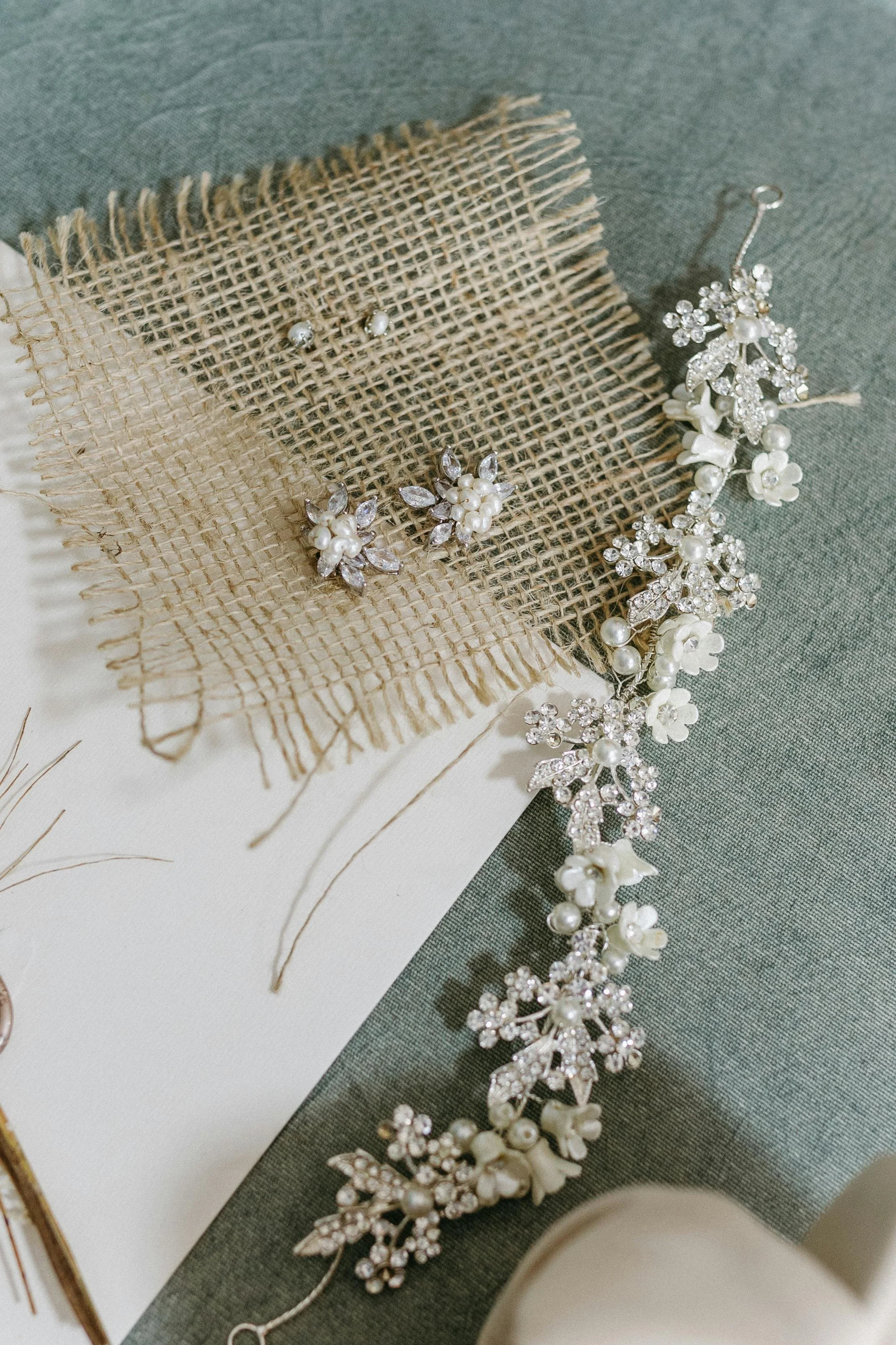 Pearl and rhinestone jewelry, including earrings and a floral headpiece or brooch, displayed on burlap and fabric backgrounds.