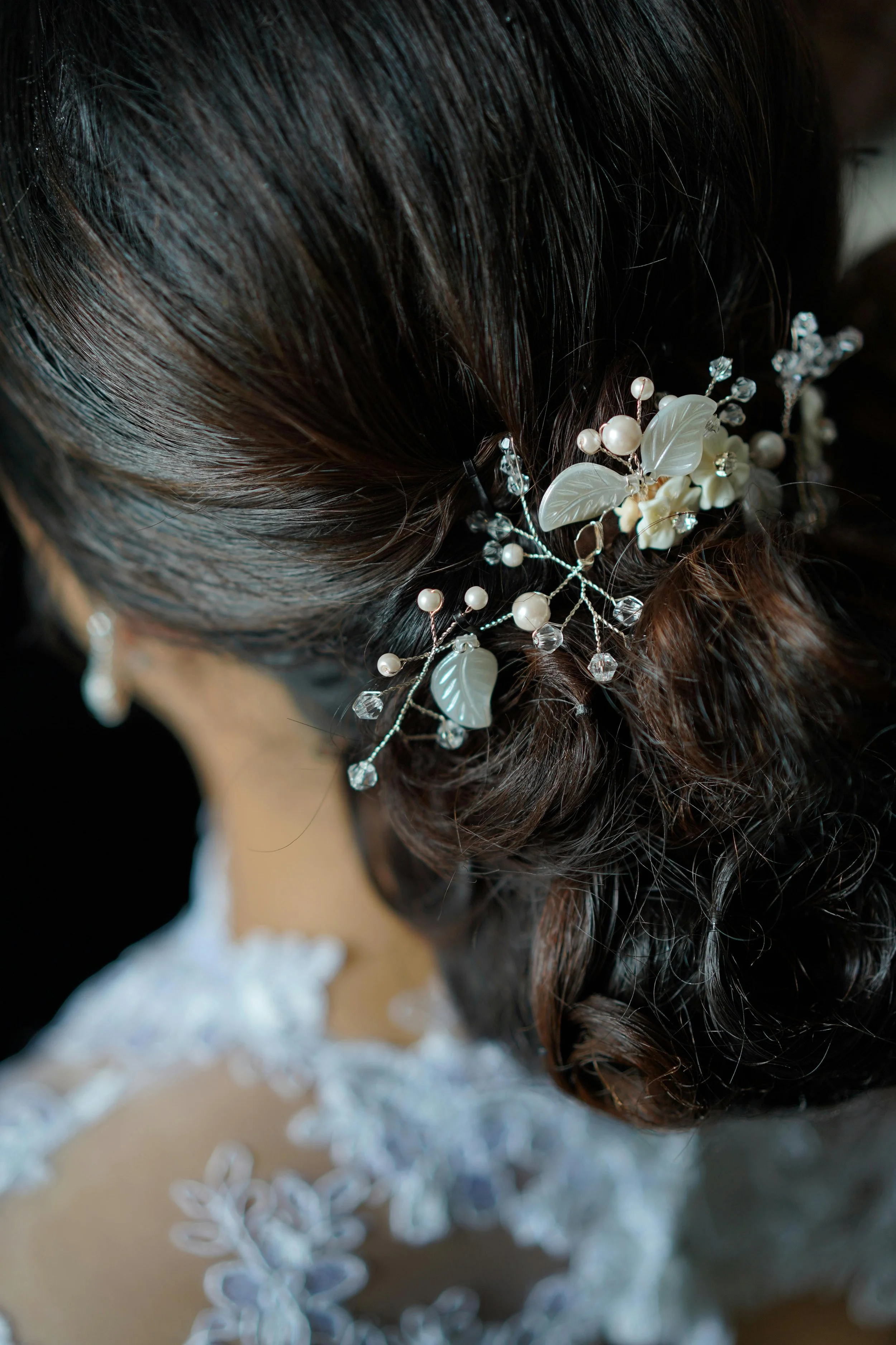 Close-up of a hairstyle decorated with pearl and crystal hair accessories, featuring dark hair with a loose curl style.