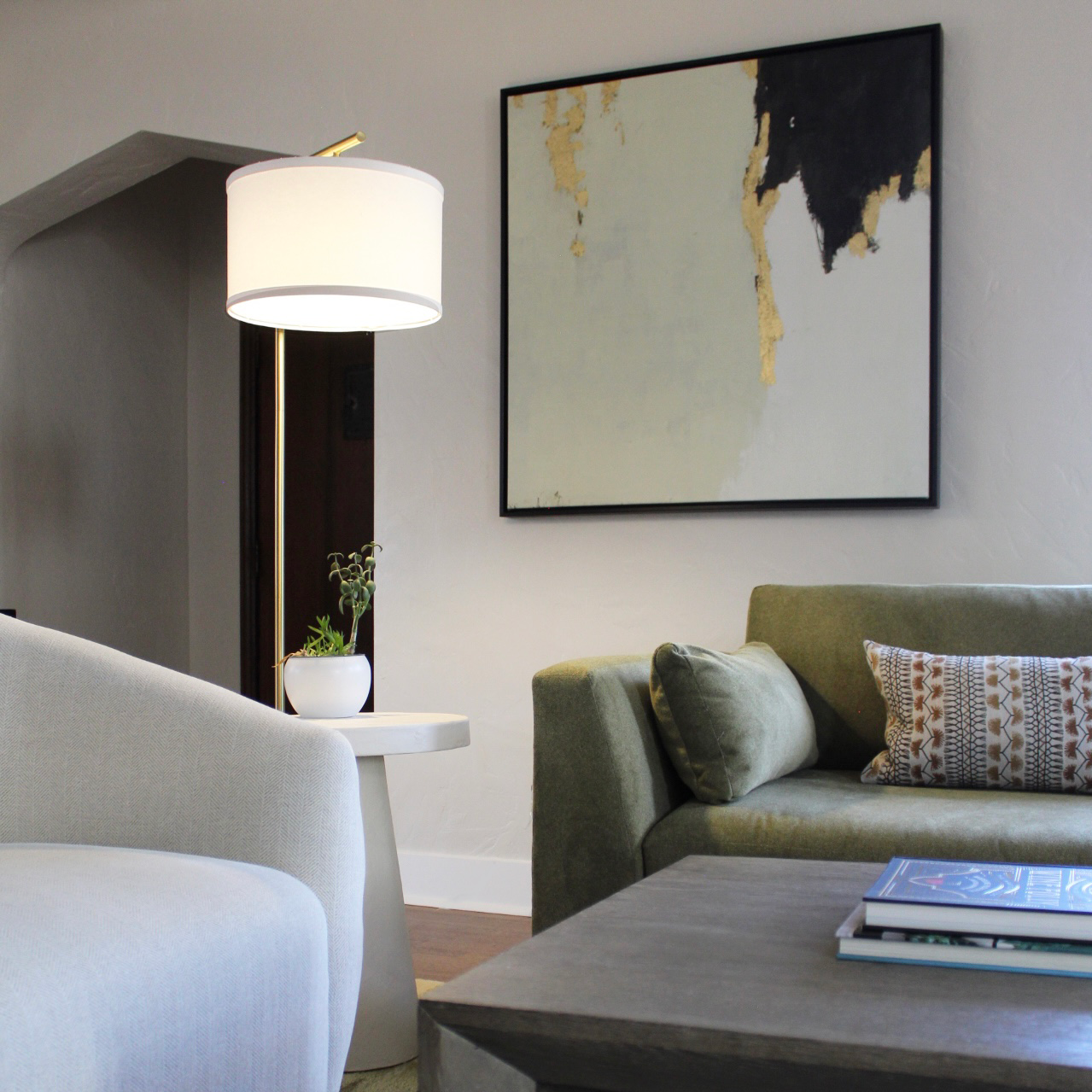 Living room with a white table lamp, green couch with pillows, abstract wall art, and a coffee table with books.