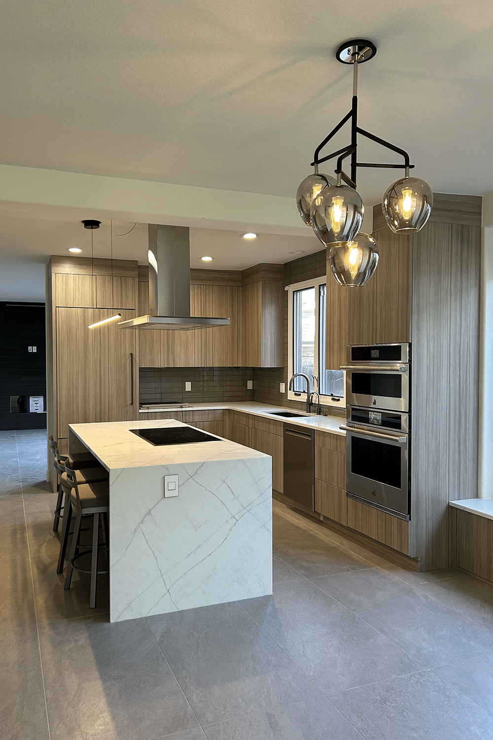 Contemporary kitchen with vertical grained cabinetry, green glass tile backsplash and stainless appliances.