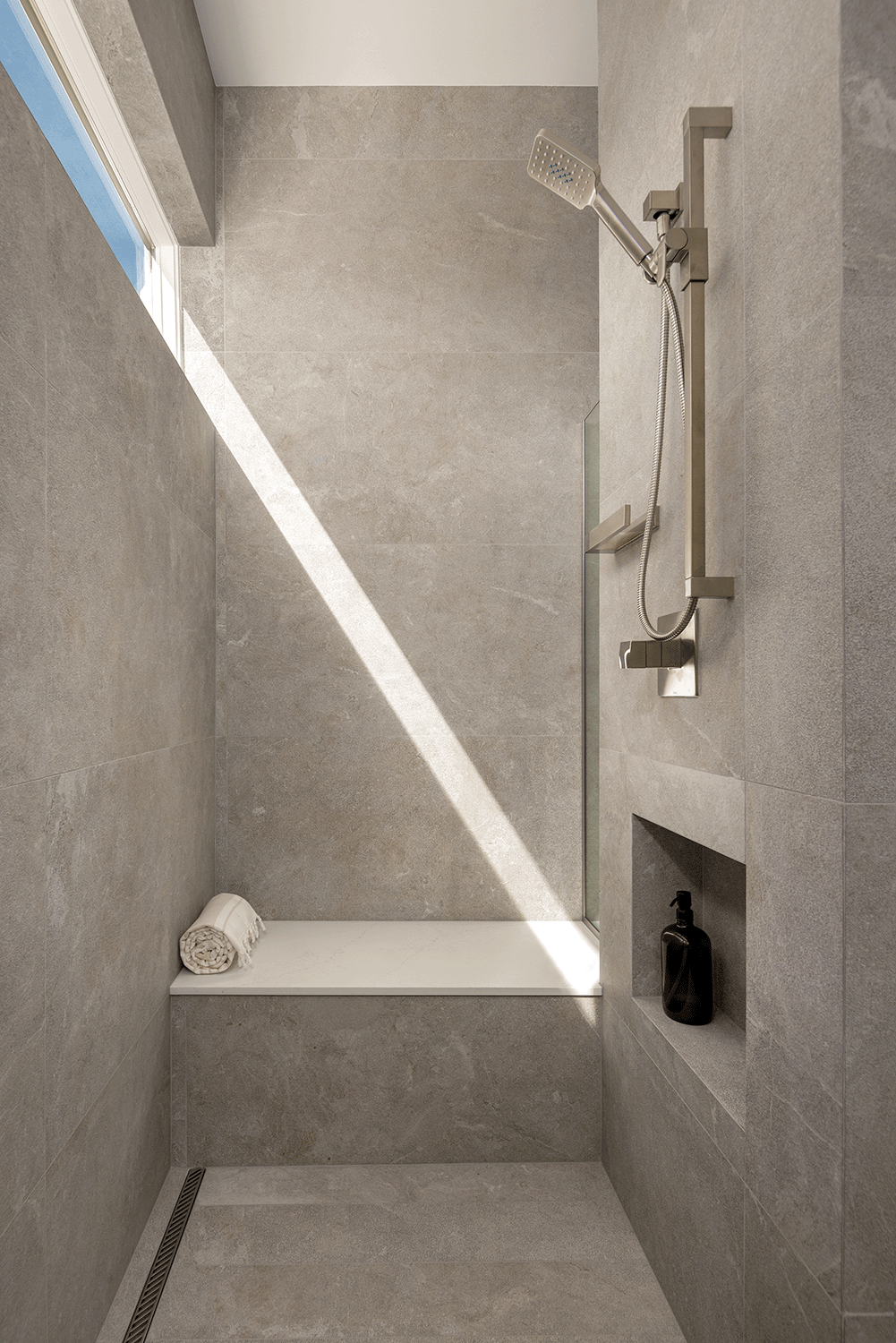 Shower bench and niche with a ray of light from the transom window angled across the wall.