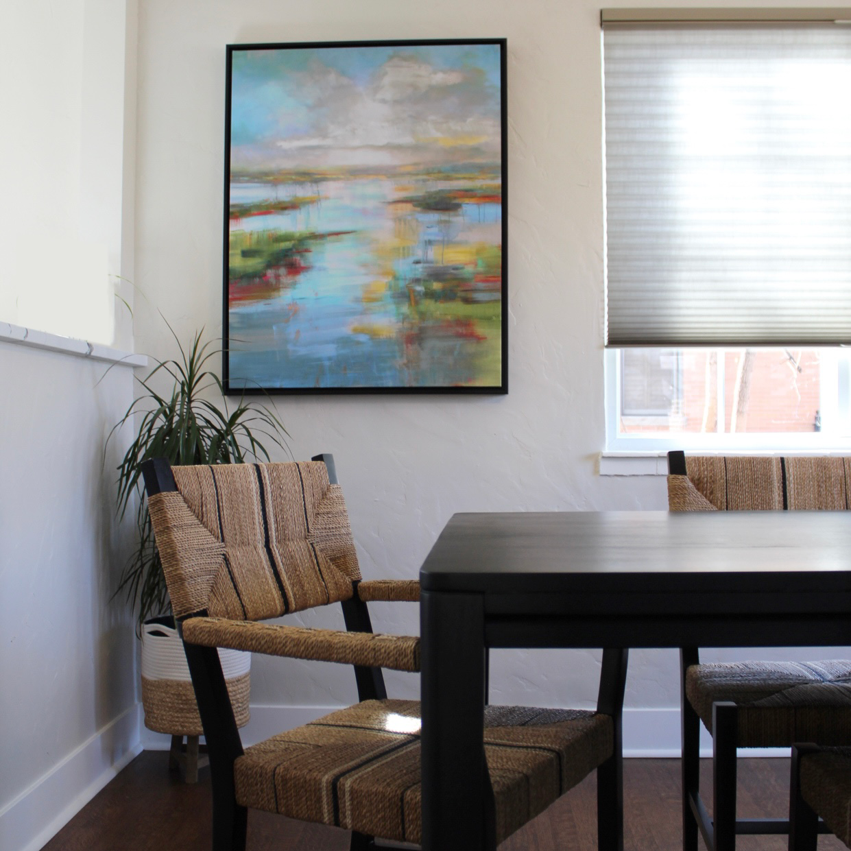 Colorful landscape artwork in a dining room with natural fiber dining chairs.