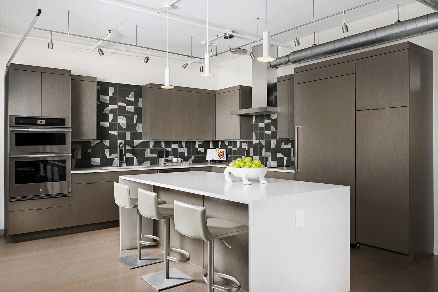 Loft kitchen featuring colorful organic patterned tile, custom cabinetry and waterfall edge island with modern pendant lighting.