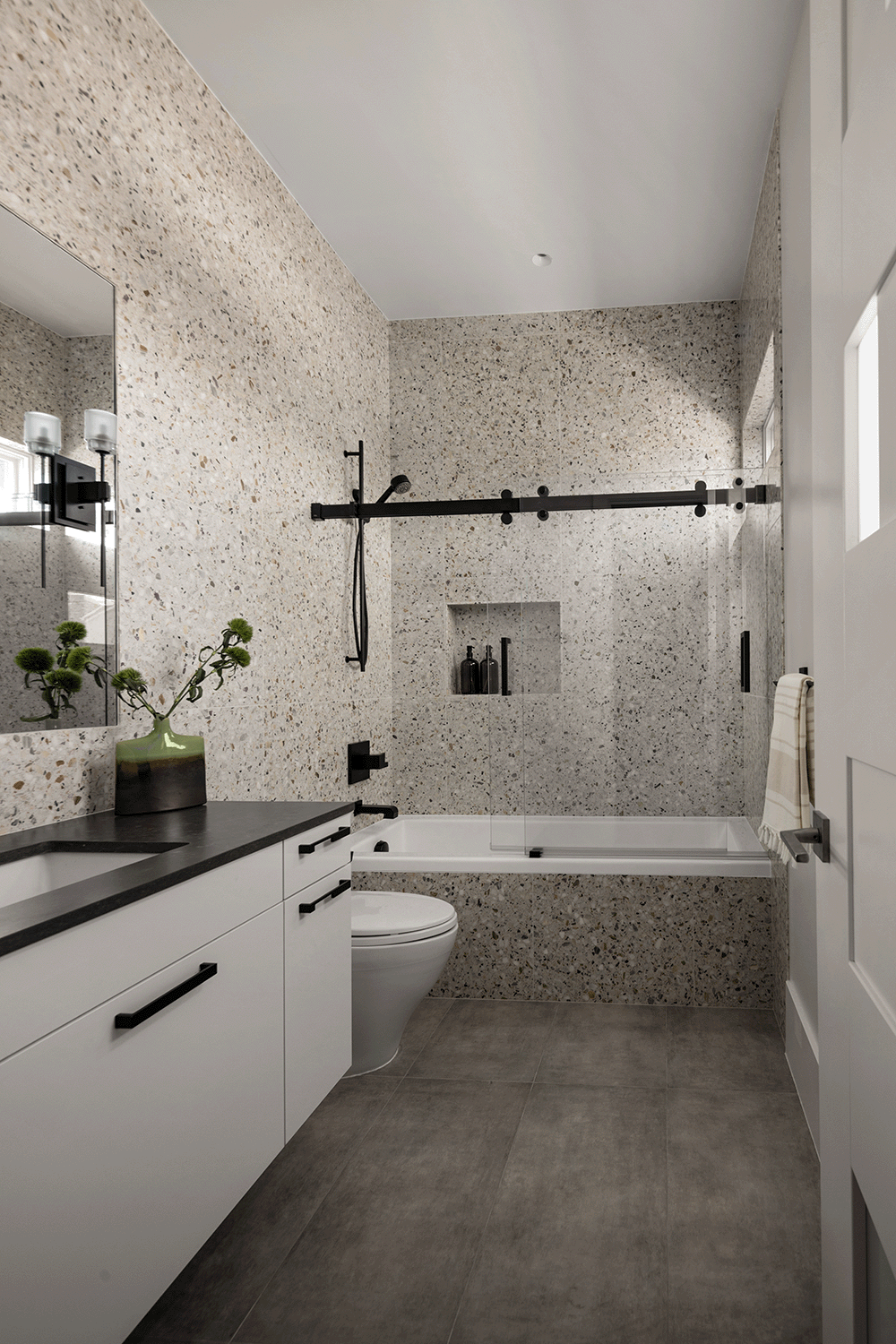 Contemporary guest bathroom with enveloped in terrazo and layered with matte black fixtures and finishes.