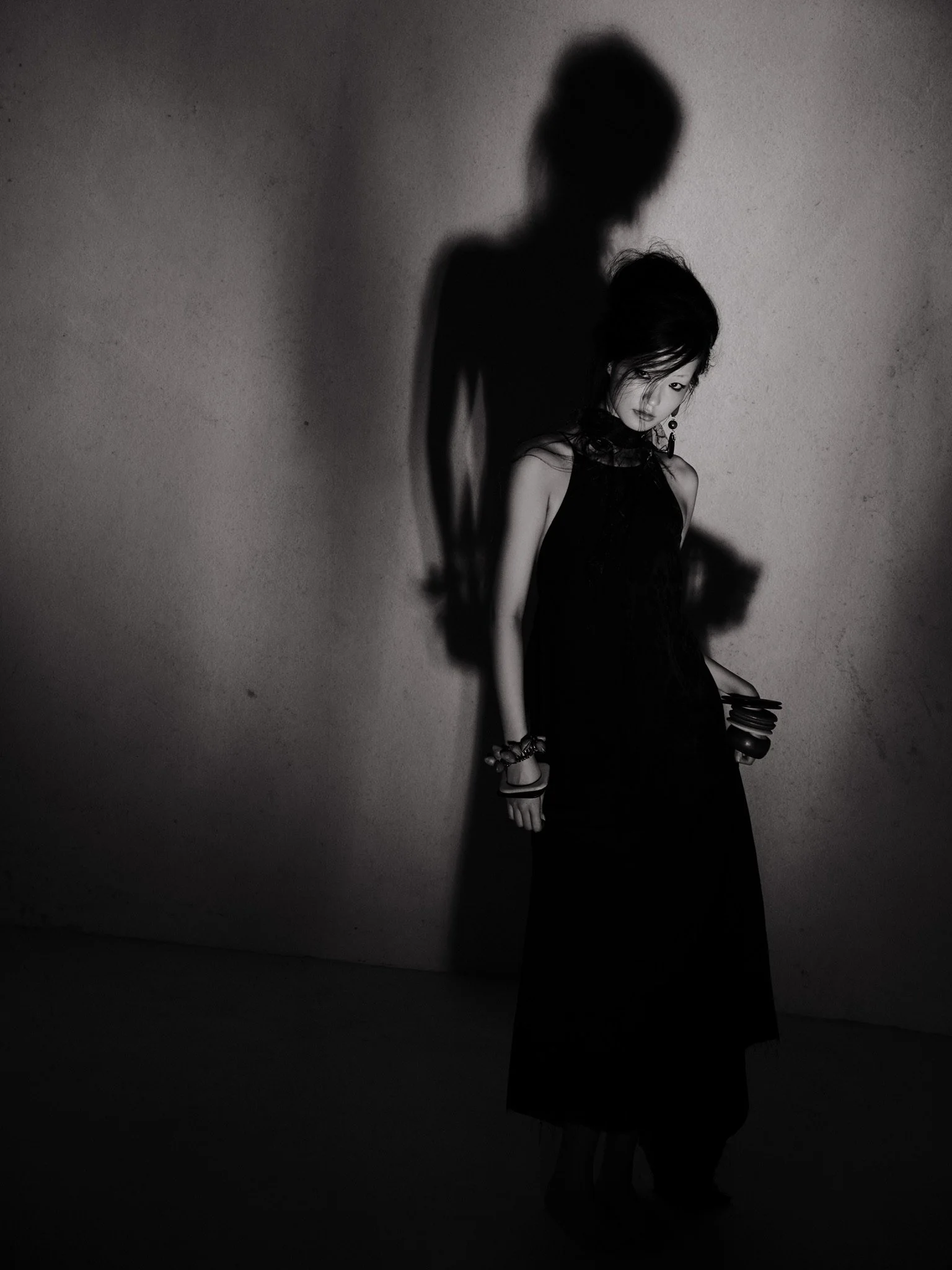 Black and white photo of a woman posing against a wall, with her shadow cast on the wall behind her.