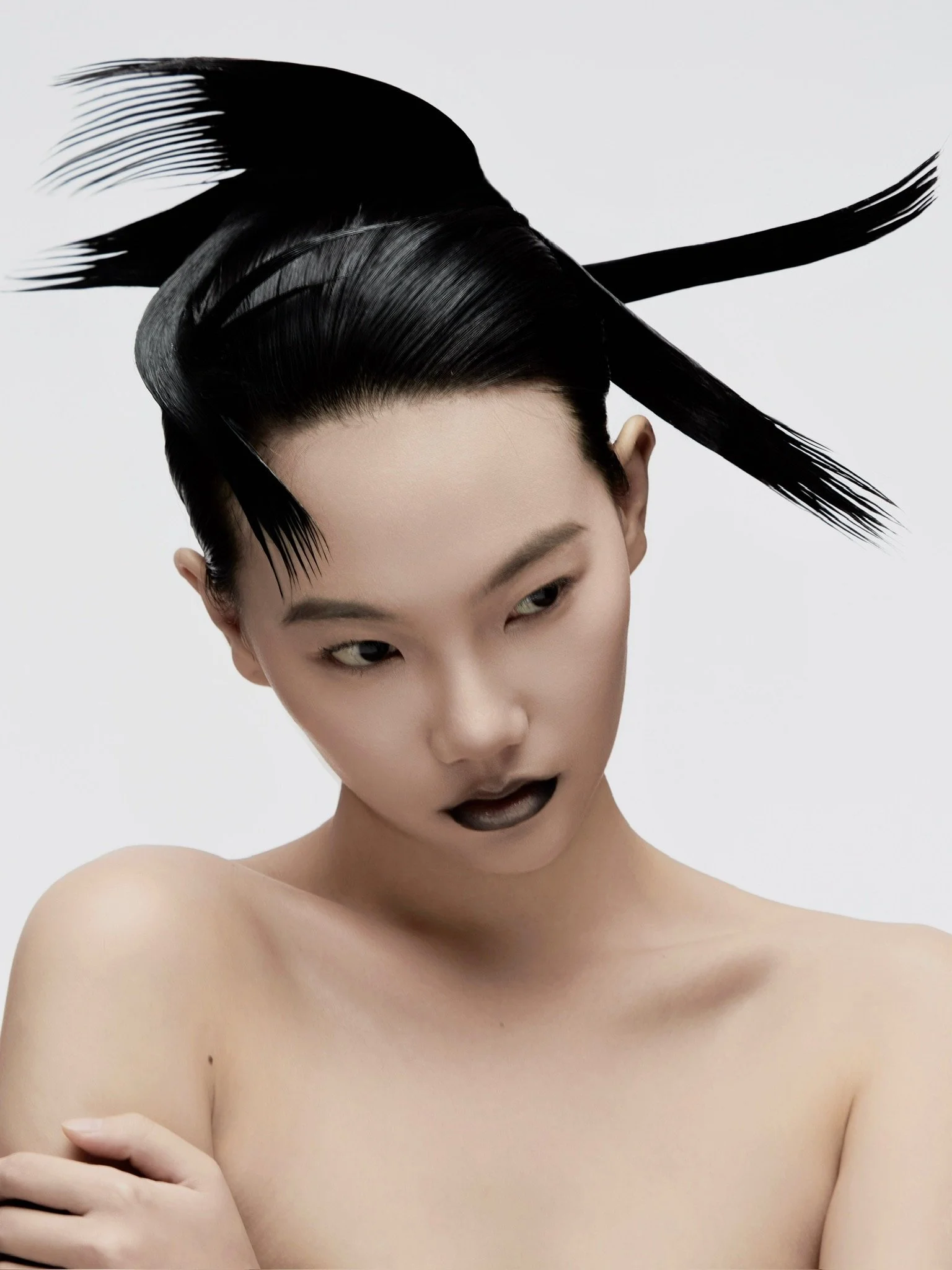 A woman with short hair and dark makeup, posing nude with crossed arms, against a plain light gray background.
