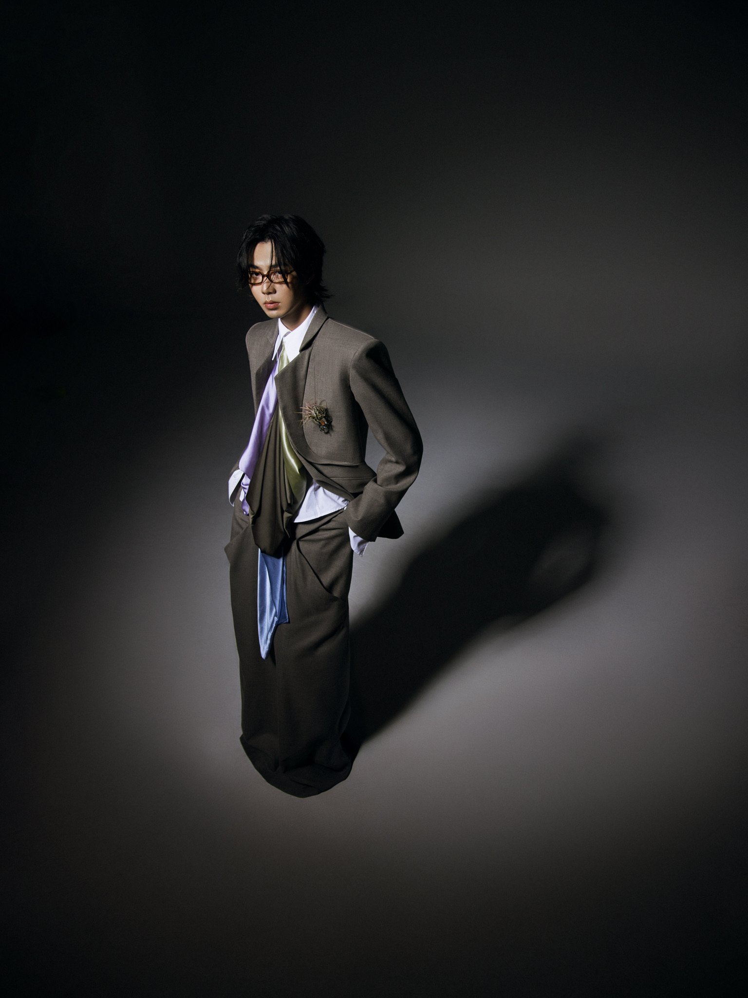 Person wearing glasses, a suit, and a tie, standing in front of a dark, gradient background.