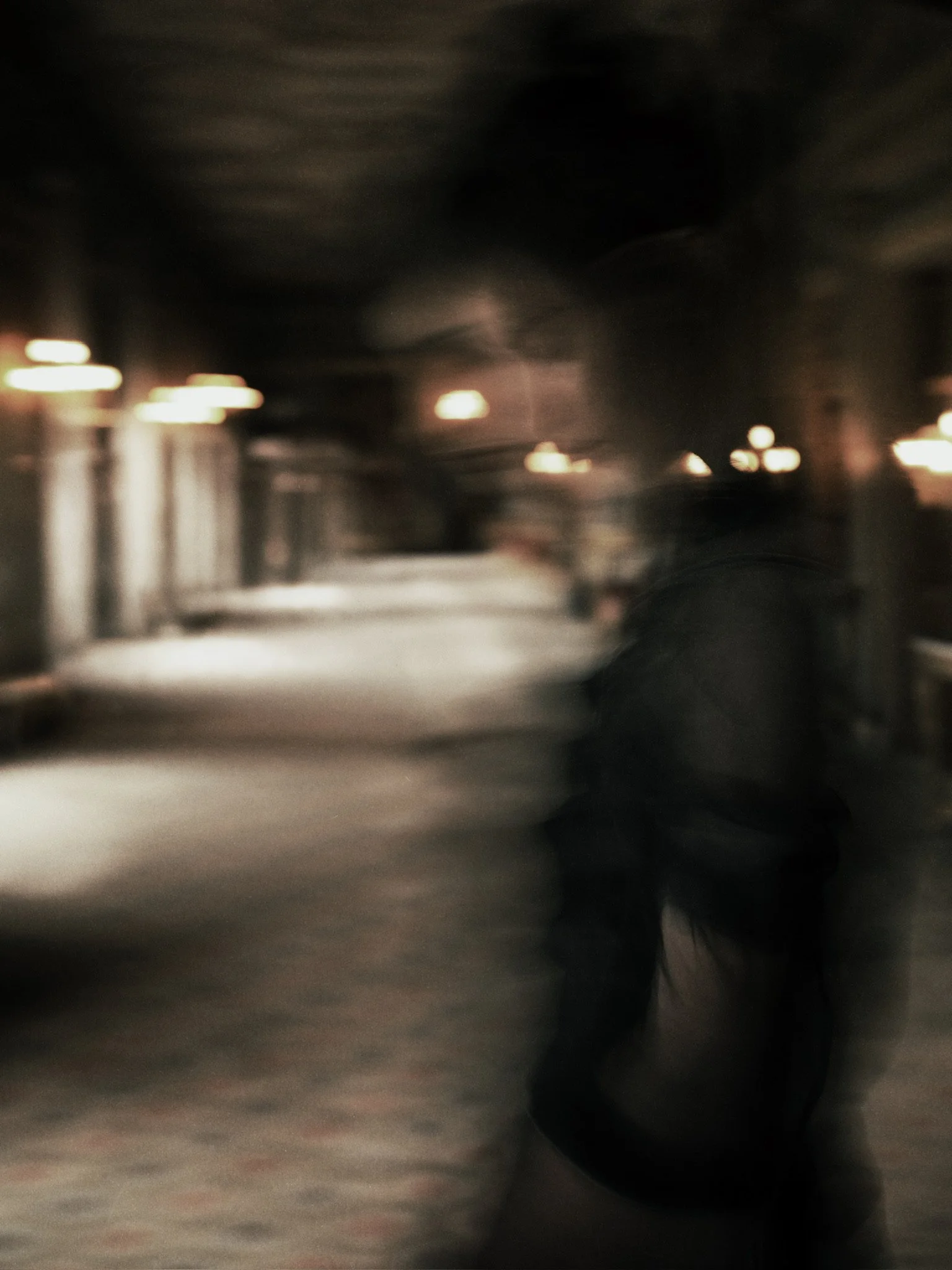 Blurry image of an indoor space with ceiling lights, walls, and a dark figure or object in the foreground.
