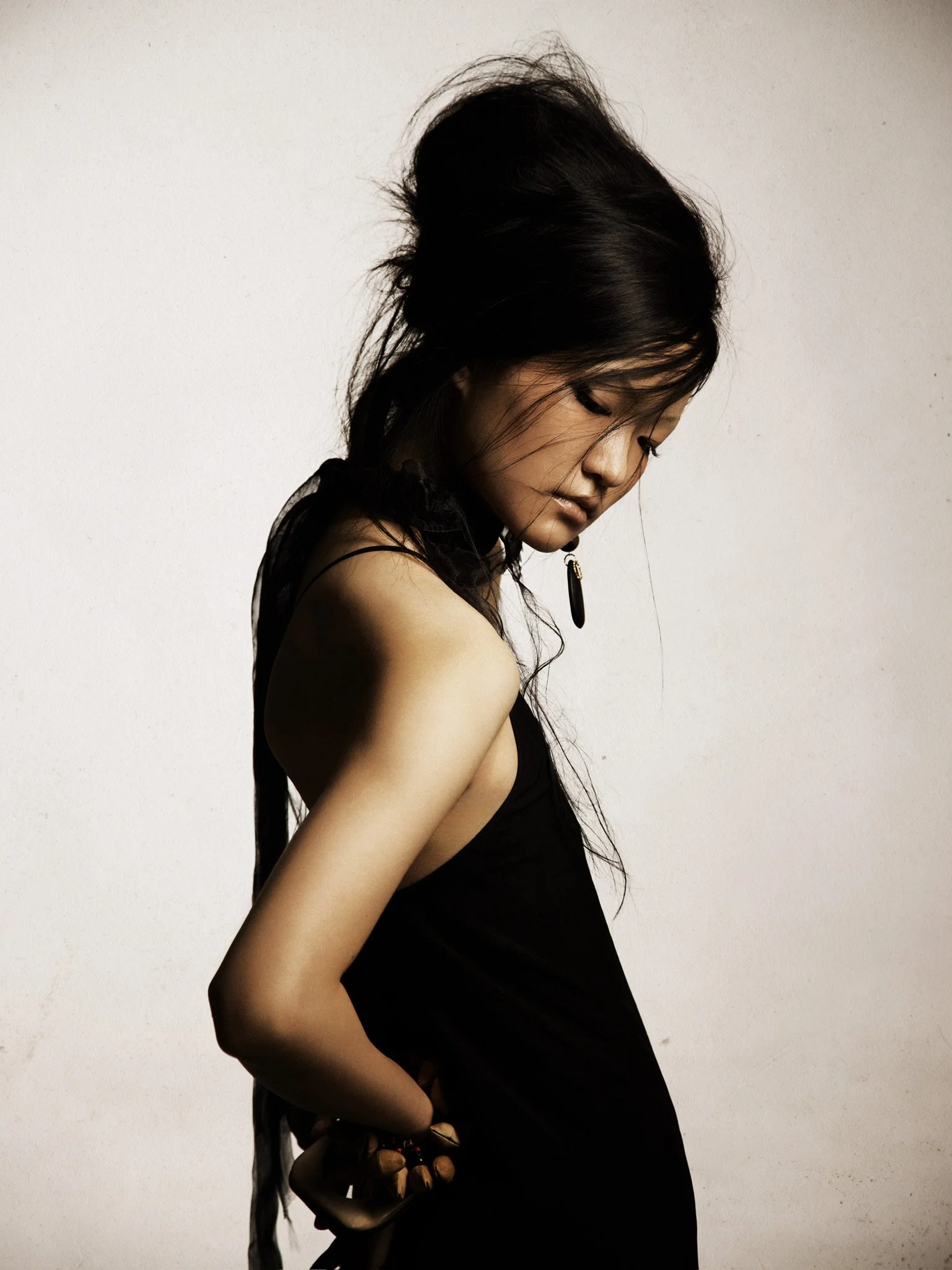 Profile of a young woman with long black hair, looking down, wearing a black sleeveless top against a plain white background.
