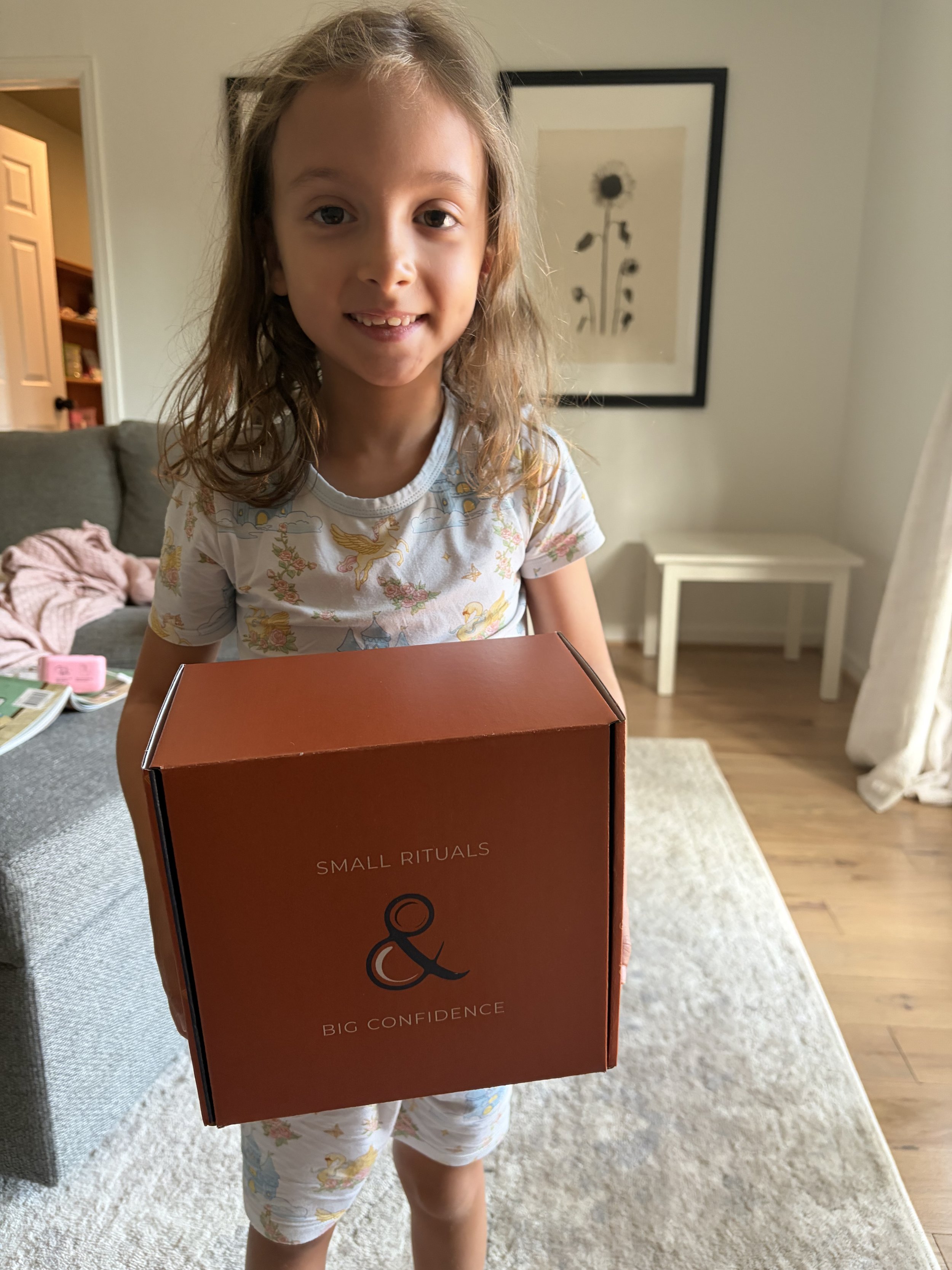Elementary age girl in pajamas at home with her Milk & Coffee Kids activity box