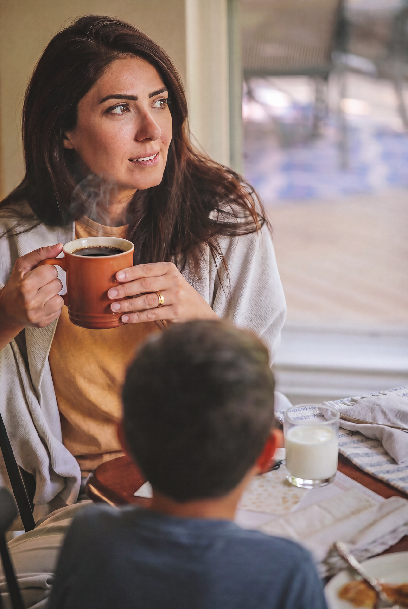 Mother holding a warm cup of coffee, sitting at a table with son in home cozy kitchen on a school day morning getting ready for first day of school.