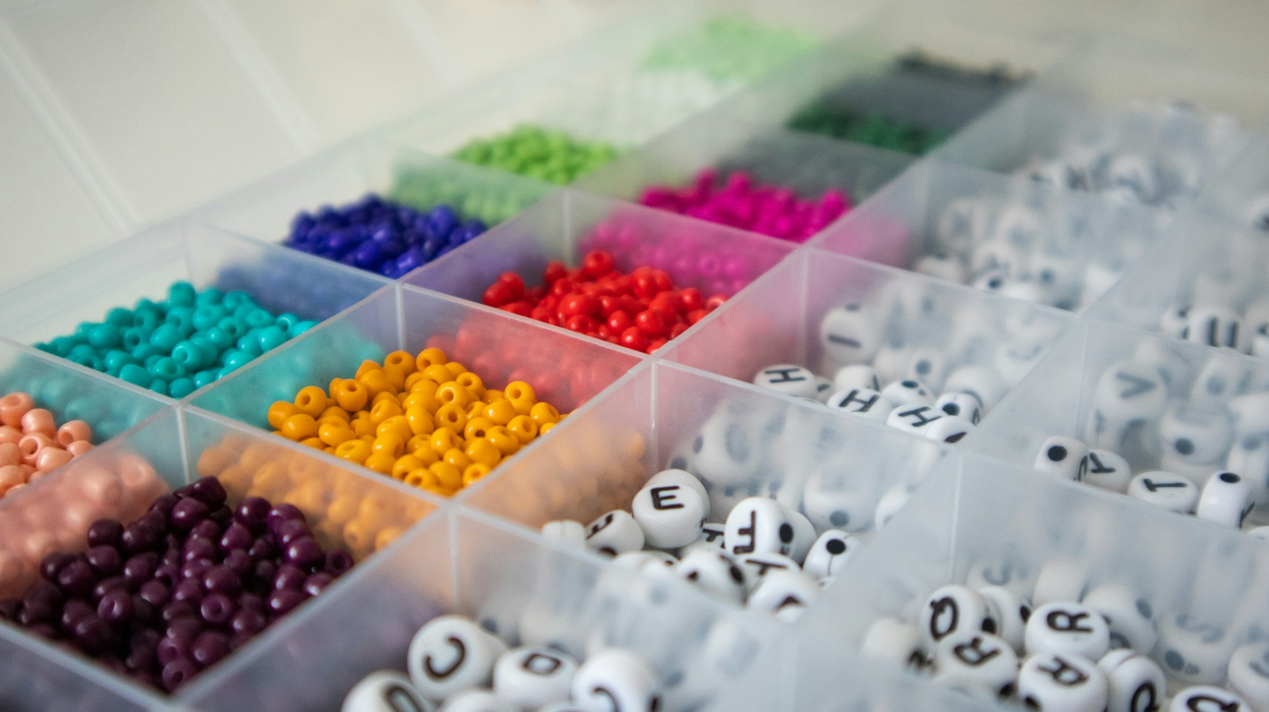 Colored beads and lettered alphabet beads organized in a plastic compartment box.