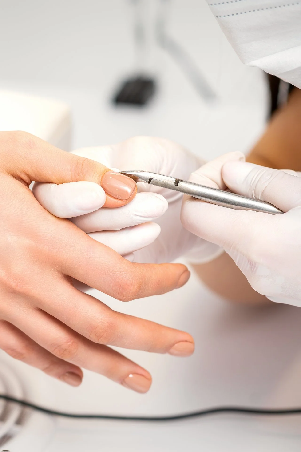 Nail technician wearing gloves applying a clear coat to a woman's fingernail with a nail polish brush.