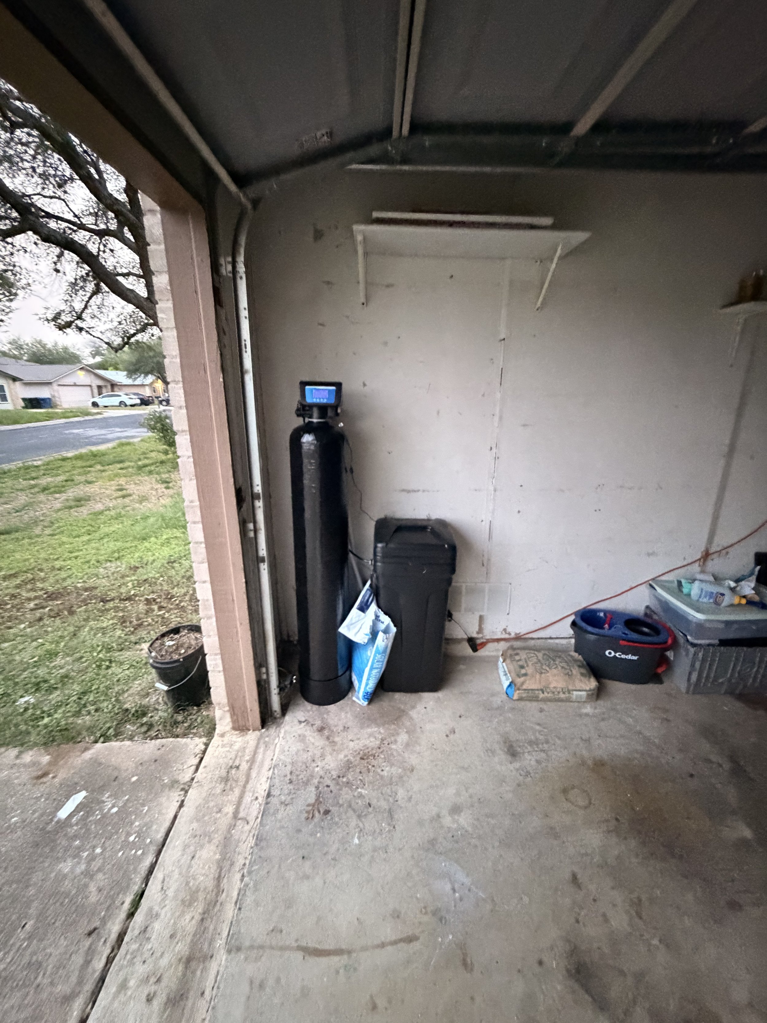 Garage interior with water filtration system, toolbox, plastic containers, and miscellaneous items on the concrete floor.