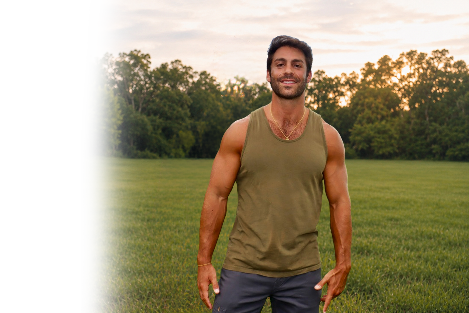 A smiling man, Andrew Zambetti, in a green sleeveless shirt and dark shorts standing in a grassy field with trees and a sunset sky in the background. The owner.