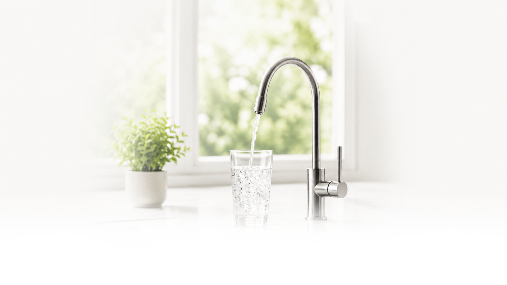 A modern kitchen sink with a stainless steel faucet running water into a glass, with a potted plant and window in the background.