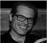 Black and white photo of a man with glasses smiling.