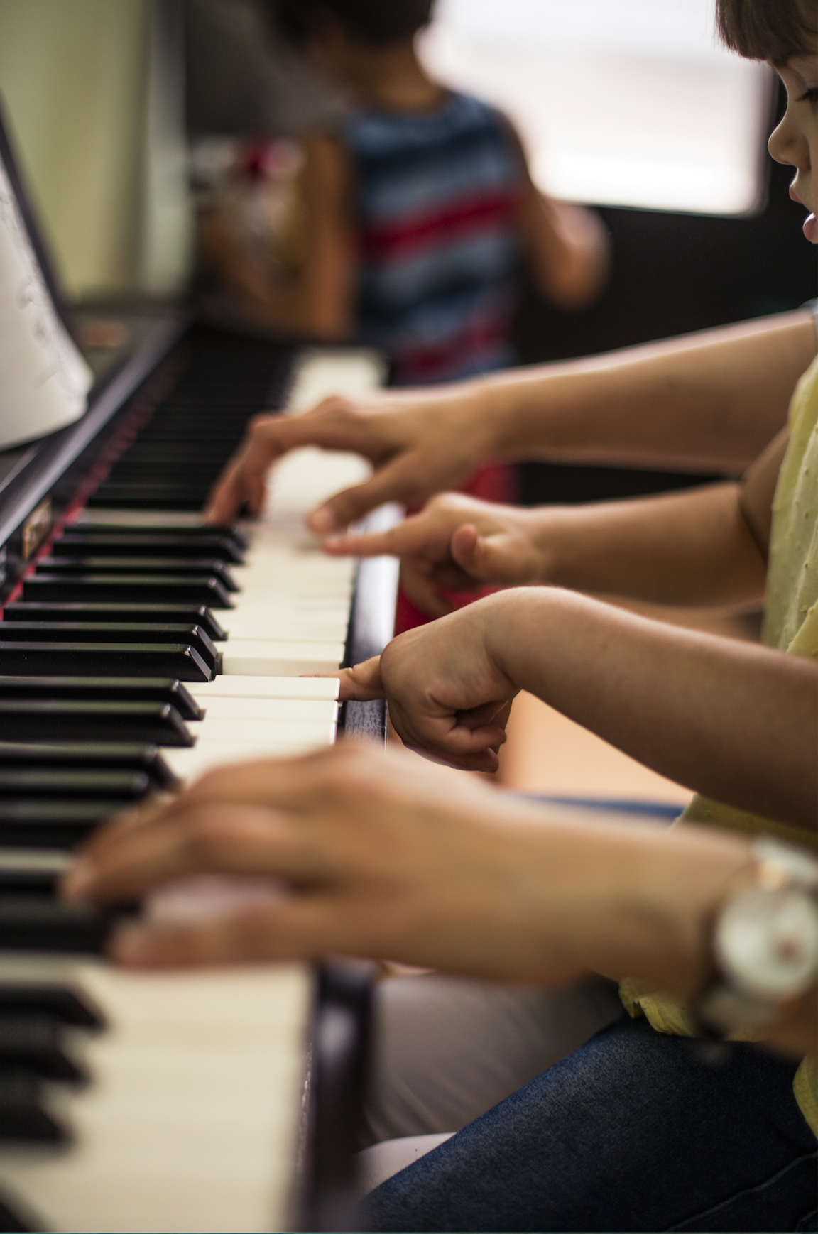 Children playing piano together in a classroom.